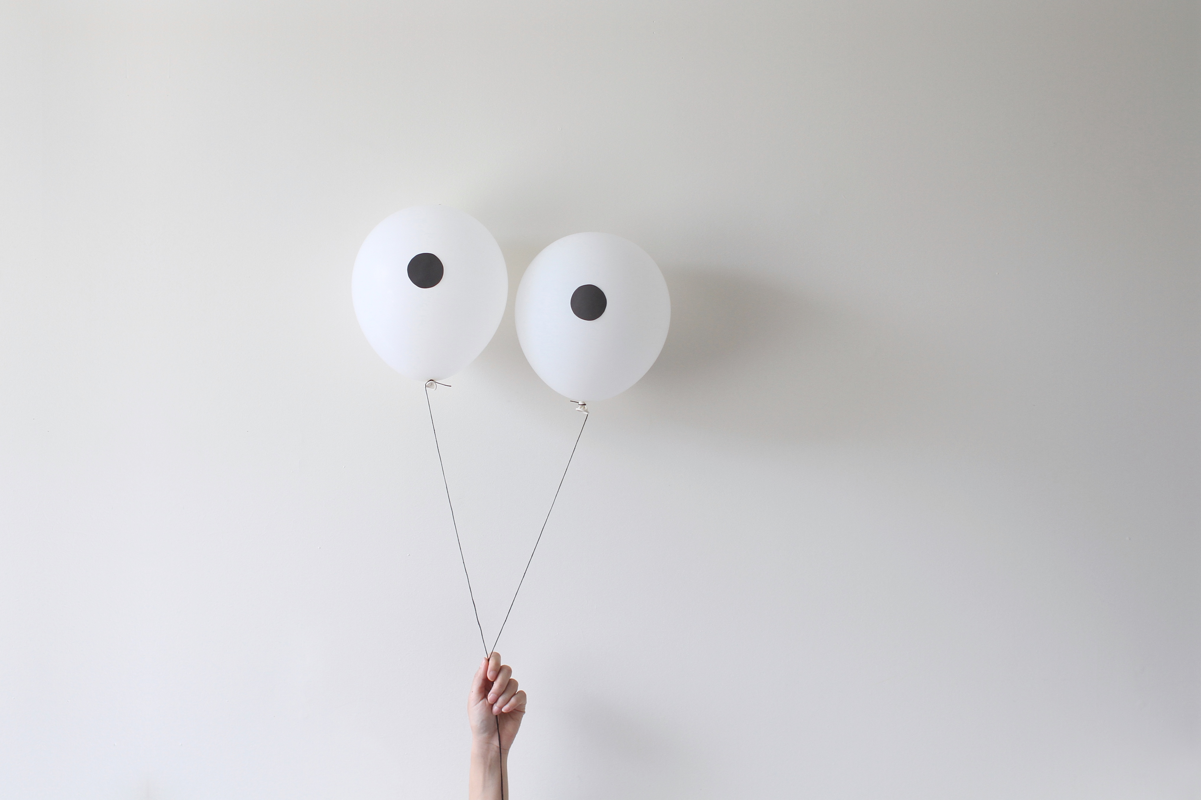 A hand holding a pair of balloons that look like eyes against a white wall