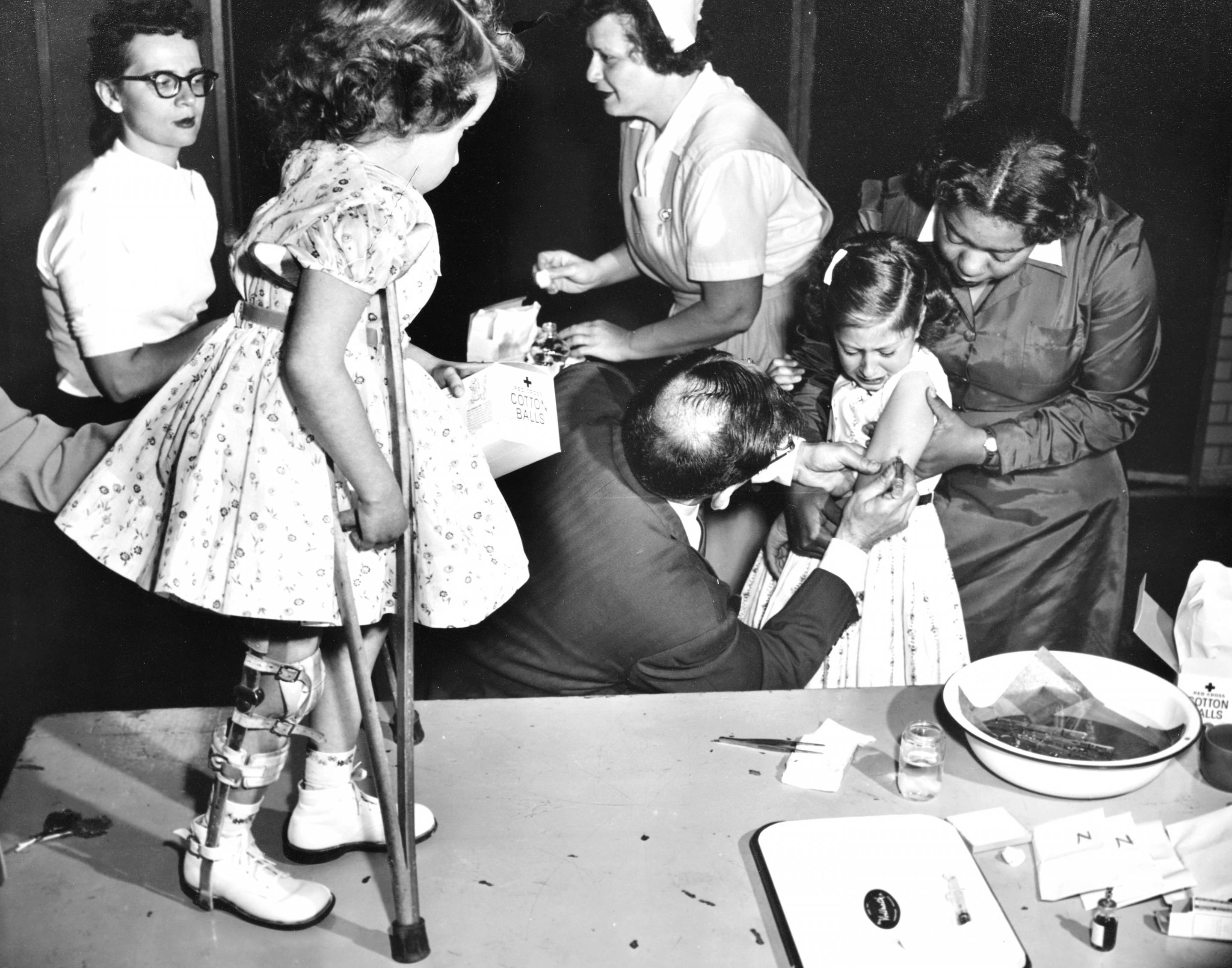 Joanne Wilson looks on as her friend Roslyn Feigenbaum gets a polio vaccine.