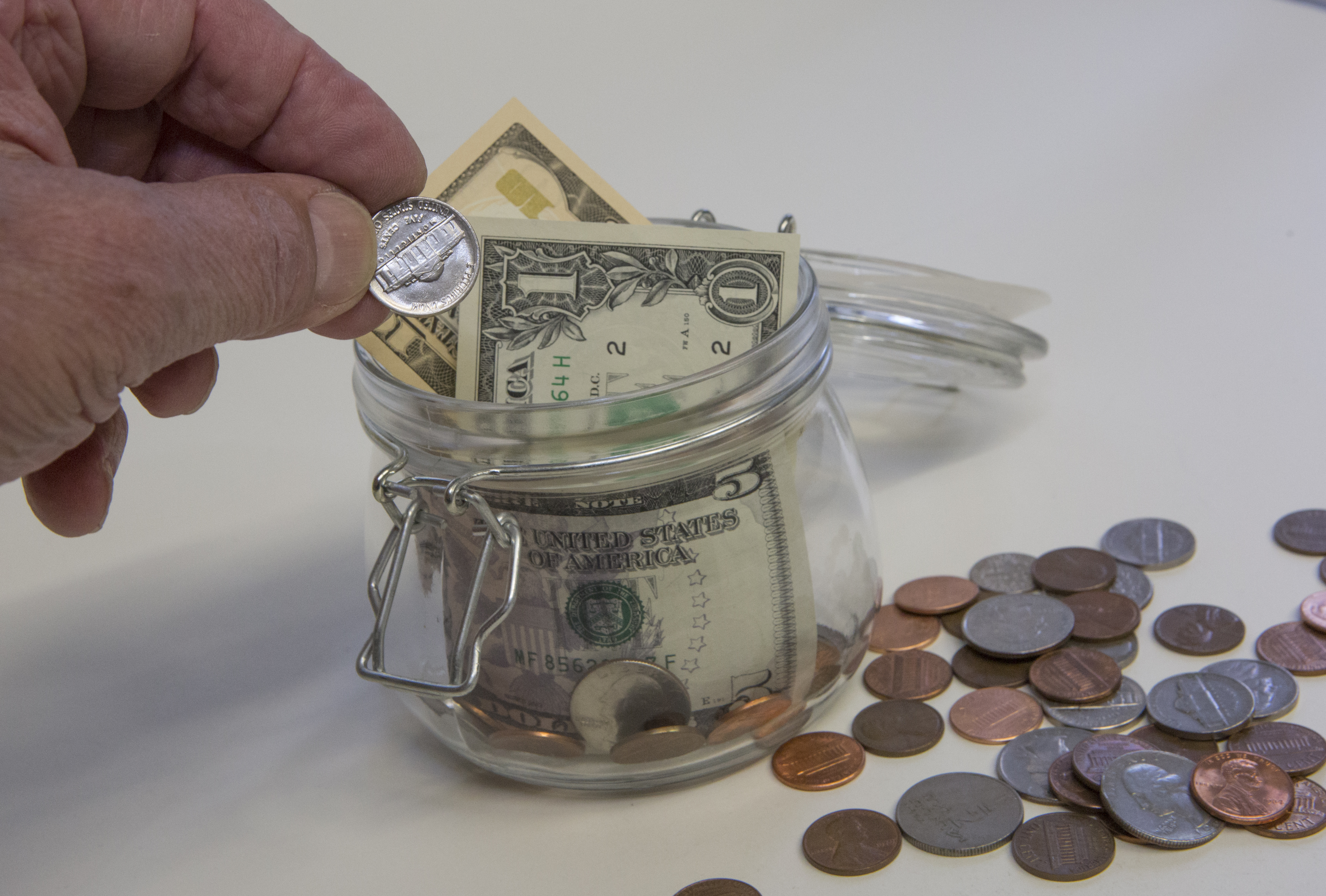 A hand drops a nickel into a savings jar