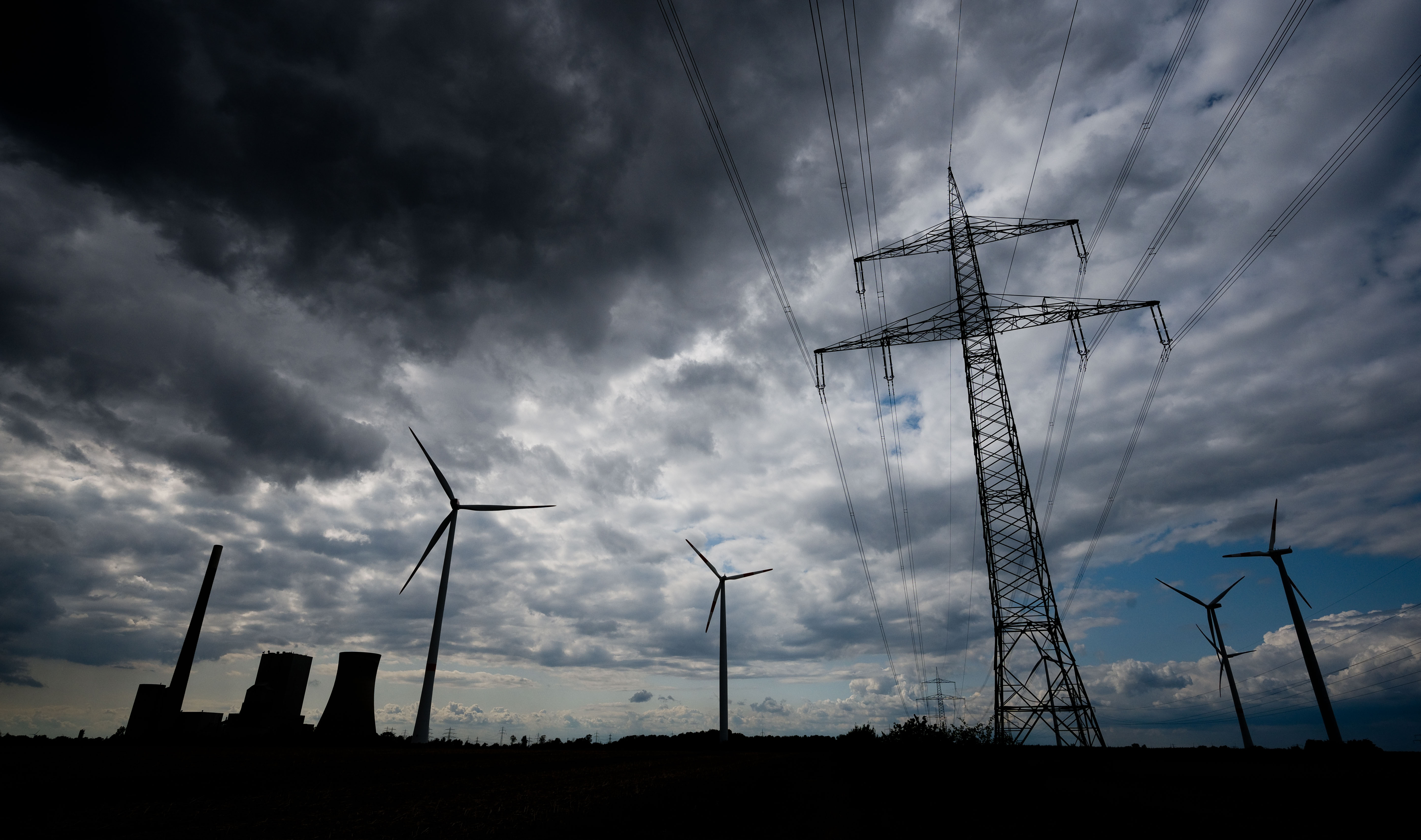 13 August 2019, Lower Saxony, Hohenhameln: Dark clouds are pulling over the Mehrum coal-fired power station, high-voltage lines and wind turbines. In view of climate change, coal-fired power plants have to be shut down quickly - a power plant near Hanover has been shut down for four months because coal-fired electricity is currently uneconomical for the operator. One reason for the low electricity price on the electricity exchange is the high share of electricity from renewable energies. Photo: Julian Stratenschulte/dpa (Photo by Julian Stratenschulte/picture alliance via Getty Images)