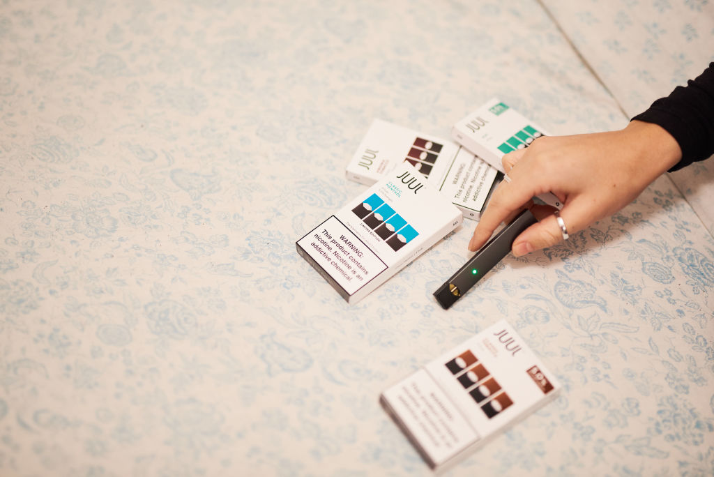 A person holds a Juul Labs Inc. e-cigarette next to packages of flavored pods in this arranged photograph taken in the Brooklyn Borough of New York, U.S., on Thursday, Dec. 20, 2018. Altria Group's plan to take a $12.8 billion stake in Juul Labs could be destroying value, Citigroup analysts write in a note downgrading the stock to a sell from neutral. Photographer: Gabby Jones/Bloomberg via Getty Images