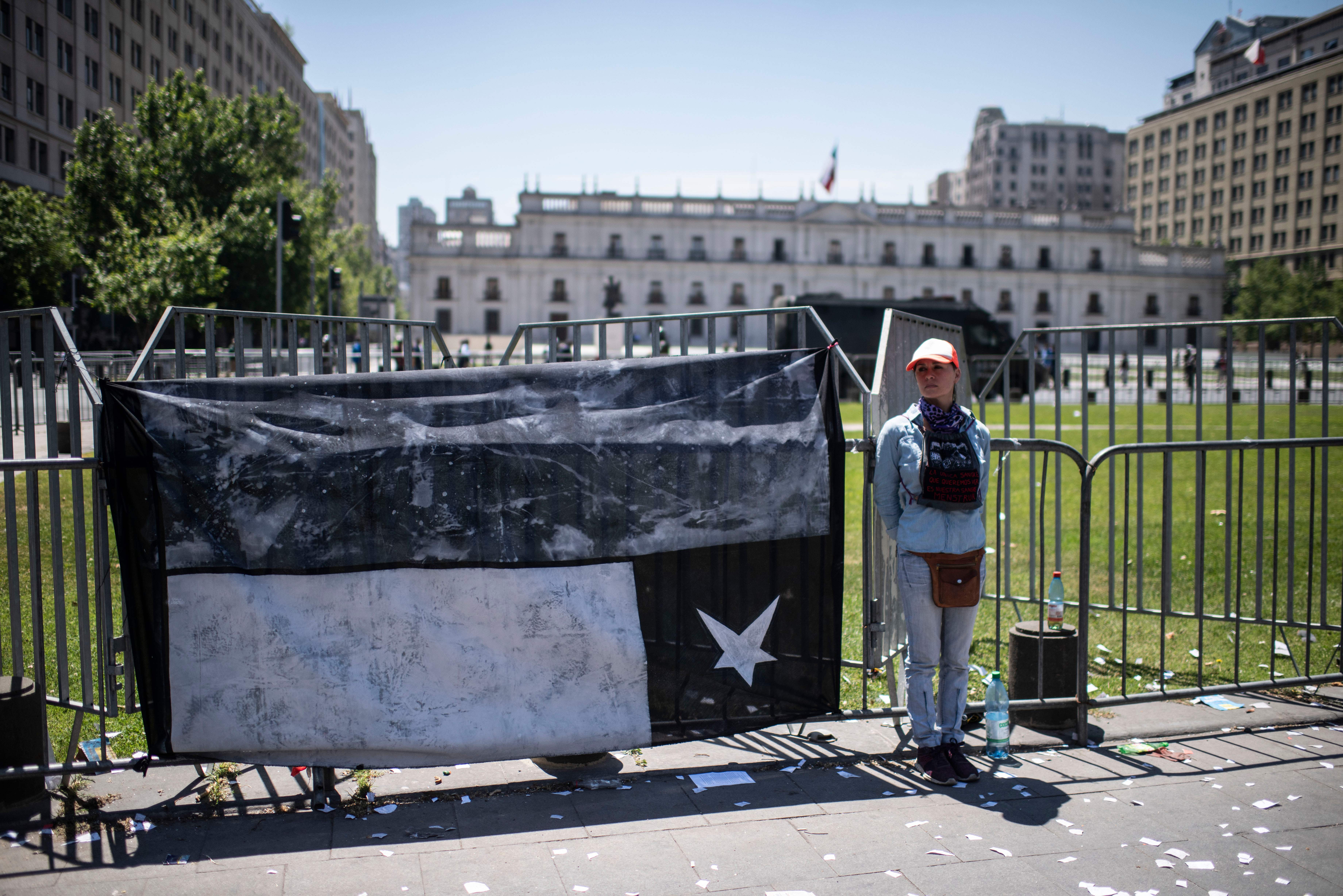 A woman stands next to an intervened Chilean national flag during a demonstration against the government economic policies in front of La Moneda presidential palace in Santiago, on October 30, 2019. - Chile pulled out of hosting two major international summits Wednesday as it struggled to restore order amid clashes between protestors and security forces that have left at least 20 dead. President Sebastian Pinera said "common sense" had dictated the decision to withdraw from the Asia Pacific Economic Cooperation summit and the Cop 25 climate change conference. (Photo by Pedro Ugarte / AFP) (Photo by PEDRO UGARTE/AFP via Getty Images)
