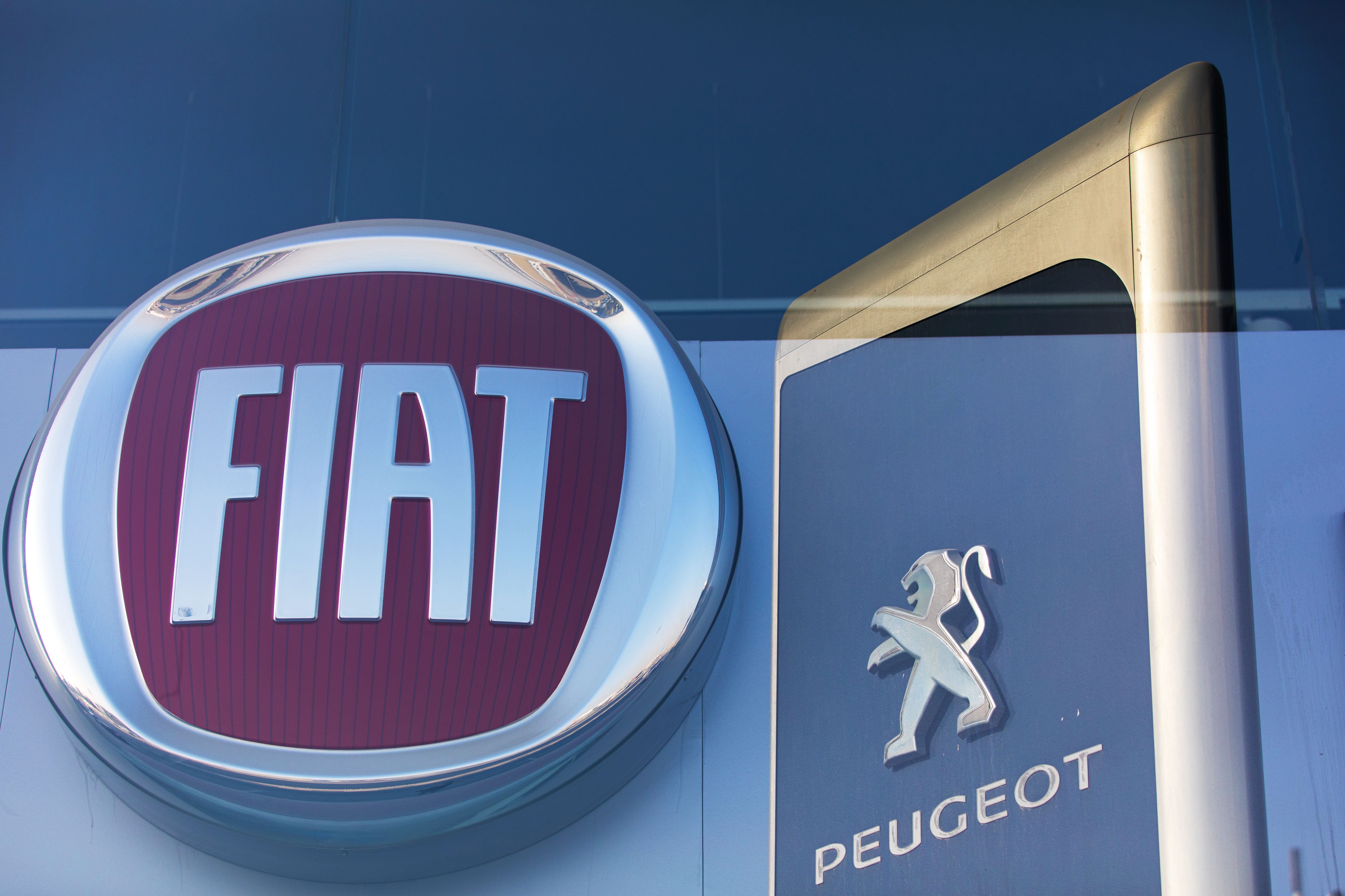 (EDITORS NOTE: Multiple exposures were combined in camera to produce this image.) The logos of Fiat Chrysler Automobiles NV and Peugeot, a unit of PSA Group, sit on display in automobile showrooms in Dubai, United Arab Emirates, on Thursday, Oct. 31, 2019. Fiat Chrysler Automobiles NV and PSA Group went out of their way to make their combination as equal as possible, shedding assets, paying special dividends and distributing board seats. It didnt take long for investors to figure out who the buyer is. Photographer: Christopher Pike/Bloomberg via Getty Images