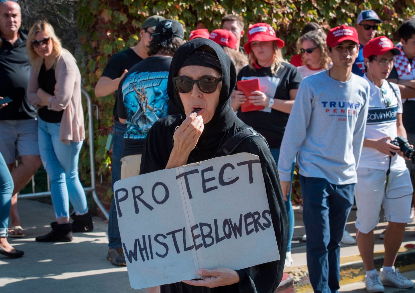 A Muslim woman holds a 'Protect Whistleblowers" sign as she walks past supporters of President Trump during a protest outside a book promotion by Donald Trump Jnr, at the UCLA campus in Westwood, California on November 10, 2019. (Photo by Mark RALSTON / AFP) (Photo by MARK RALSTON/AFP via Getty Images)