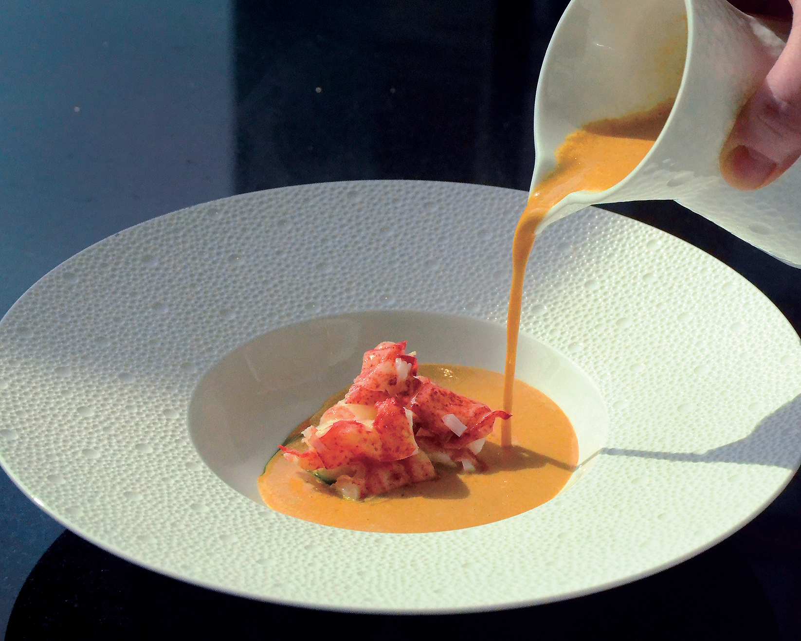 Rich lobster soup with curry: Intense lobster stock reduction finished with cream, butter-poached lobster, and curry oil.