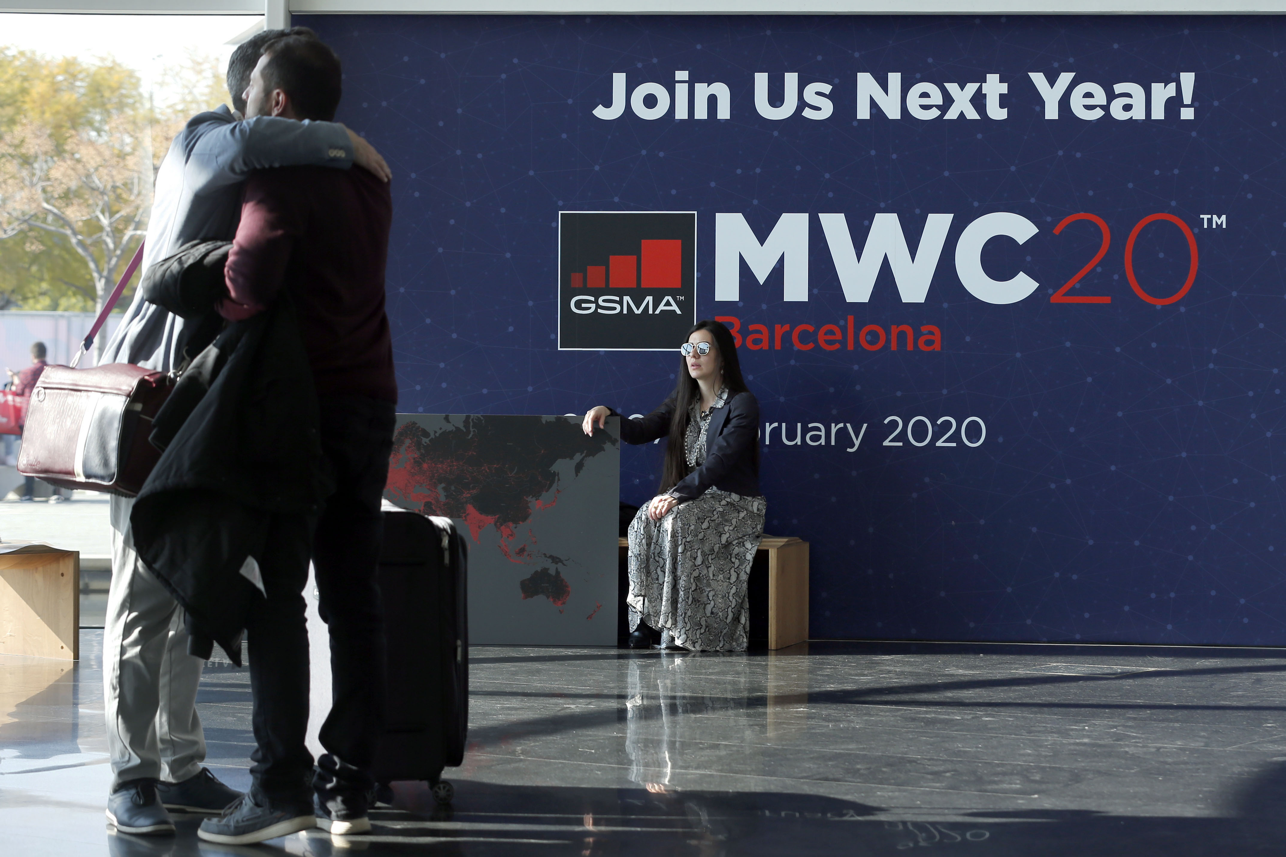 A woman looks at two visitors hugging each other on the last day of the Mobile World Congress (MWC) in Barcelona on February 28, 2019.