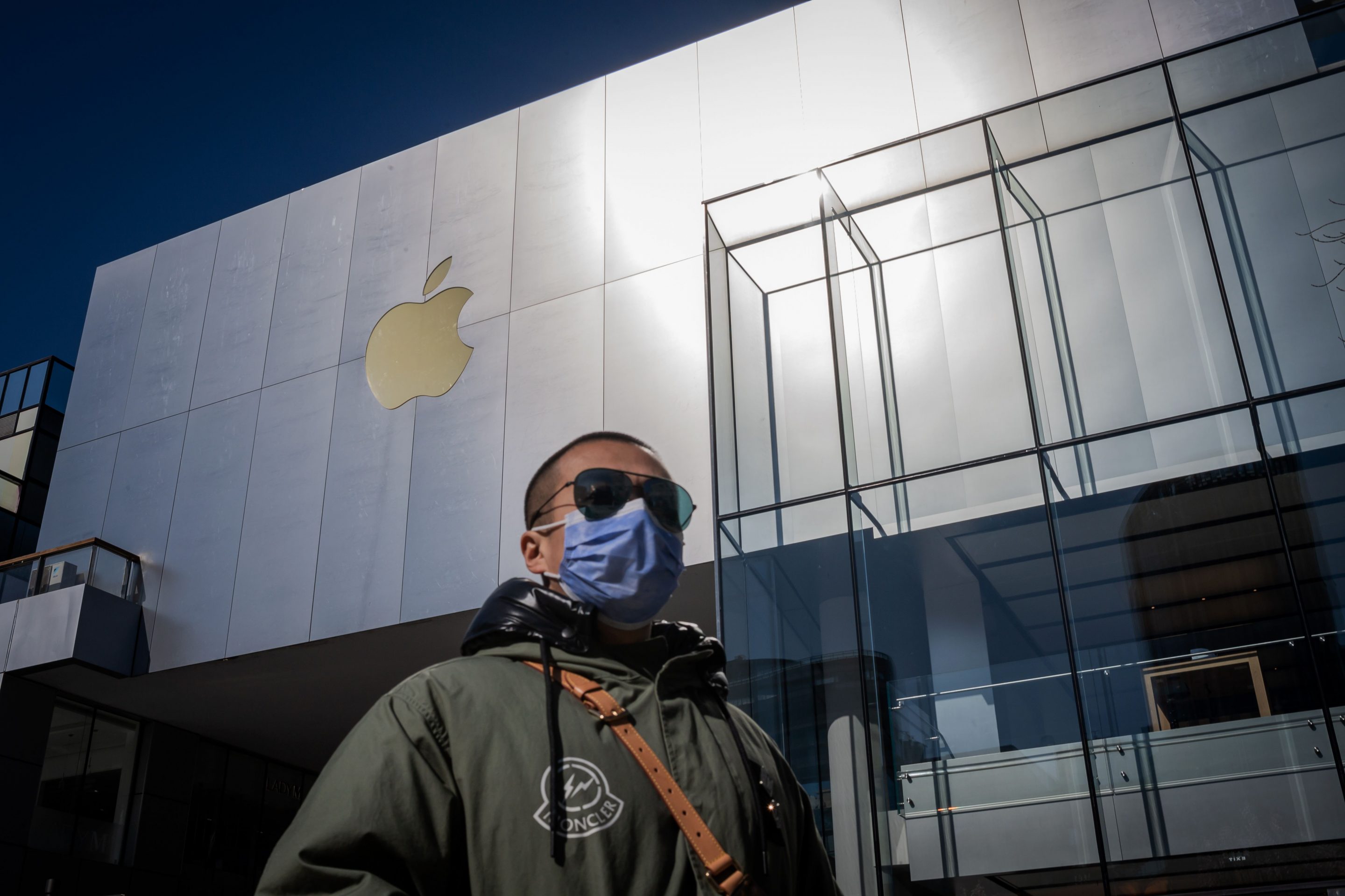 A man wearing a facemask to protect against the COVID-19 coronavirus walks outside an Apple Store in Beijing on February 22, 2020. - The US tech giant said in a statement February 18 its revenue for the current quarter would be below its forecasts, and that worldwide iPhone supply "will be temporarily constrained" because of the global virus outbreak, notably in China where Apple manufactures most of its devices.  