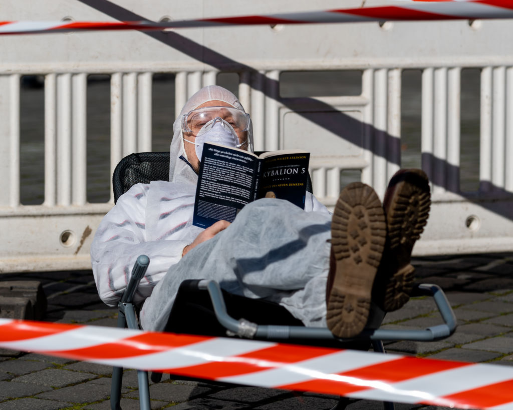 A resident lies on a sun lounger in protective clothing and with a mask behind barrier tape on Neumarkt in front of the Frauenkirche and reads a book. To contain the coronavirus, Saxony now bans all gatherings of three or more people in public. Dresden, Germany. March 23, 2020,