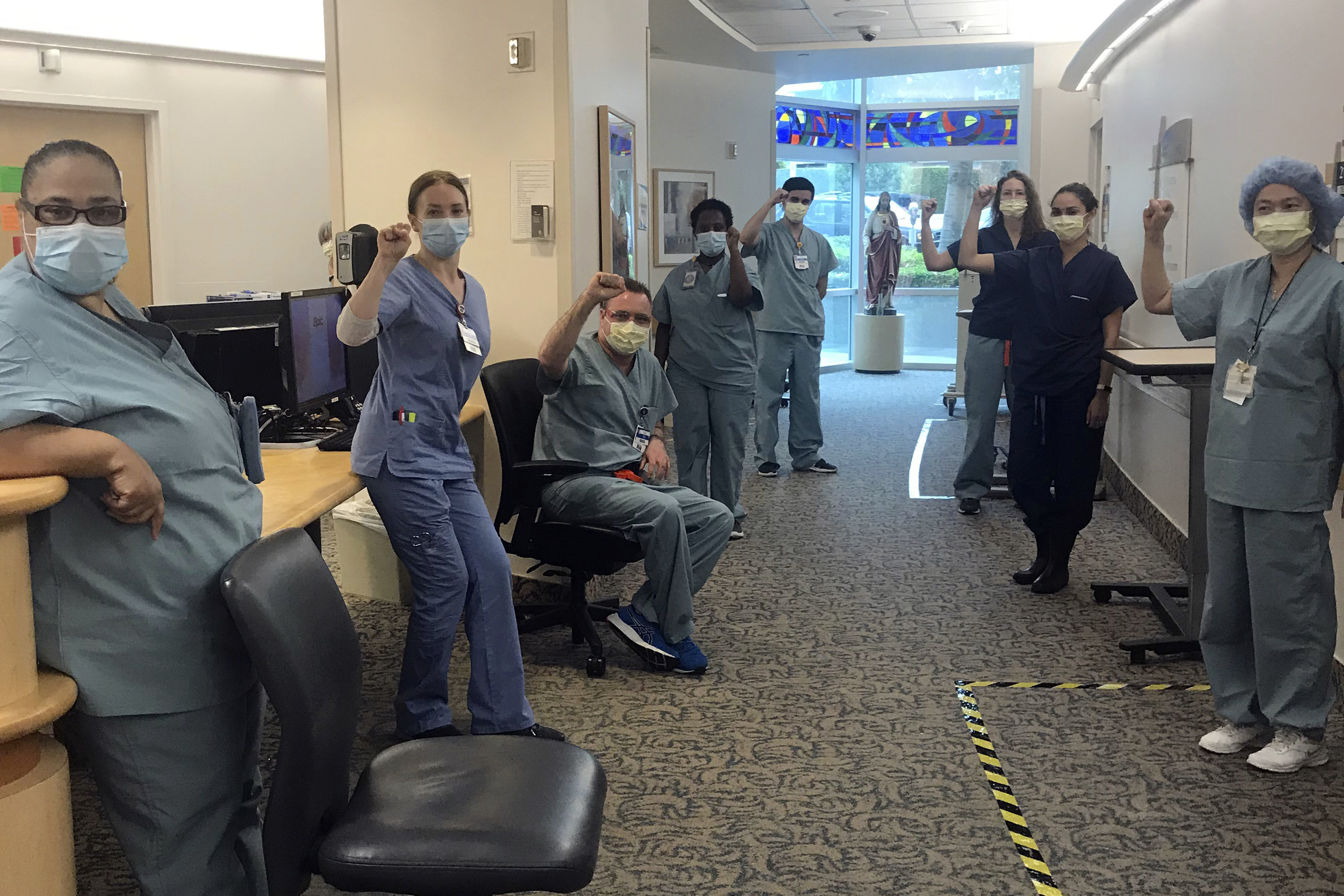 In this image provided by Lizabeth Baker Wade, nurses at Providence Saint John's Health Center in Santa Monica, Calif., on April 10, 2020, raise their fists in solidarity after telling managers they can't care for COVID-19 patients without N95 respirator masks to protect themselves. The hospital has suspended ten nurses from the ward, but has started providing nurses caring for COVID-19 patients with N95 masks. (Lizabeth Baker Wade via AP)