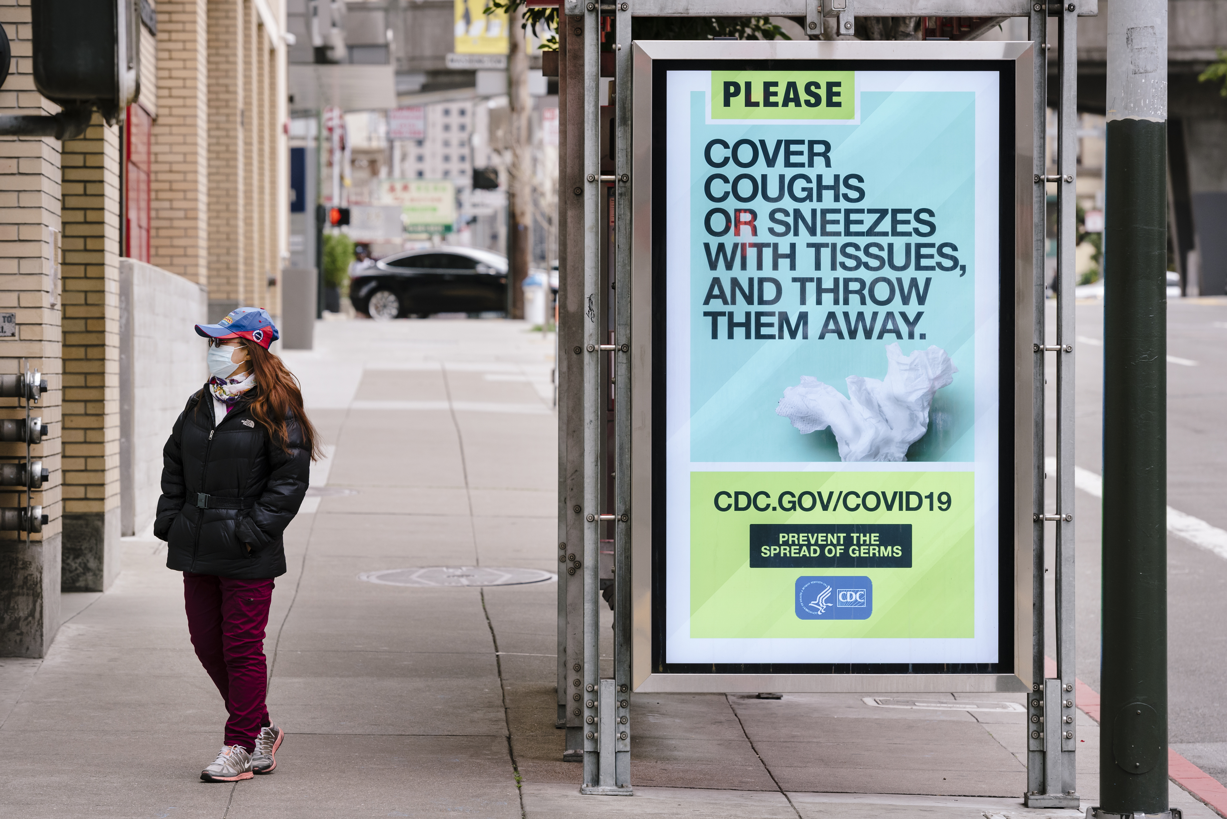 A pedestrian wearing a face mask stands next to a MUNI bus stop displaying an advertisement placed by the Centers for Disease Control (CDC) on the coronavirus in San Francisco, California, U.S., on Friday, March 20, 2020. California Governor Gavin Newsom ordered that all of the states 40 million residents go into home isolation starting Thursday evening, marking the most stringent U.S. effort yet to stymie the spread of the novel coronavirus. Photographer: Michael Short/Bloomberg via Getty Images