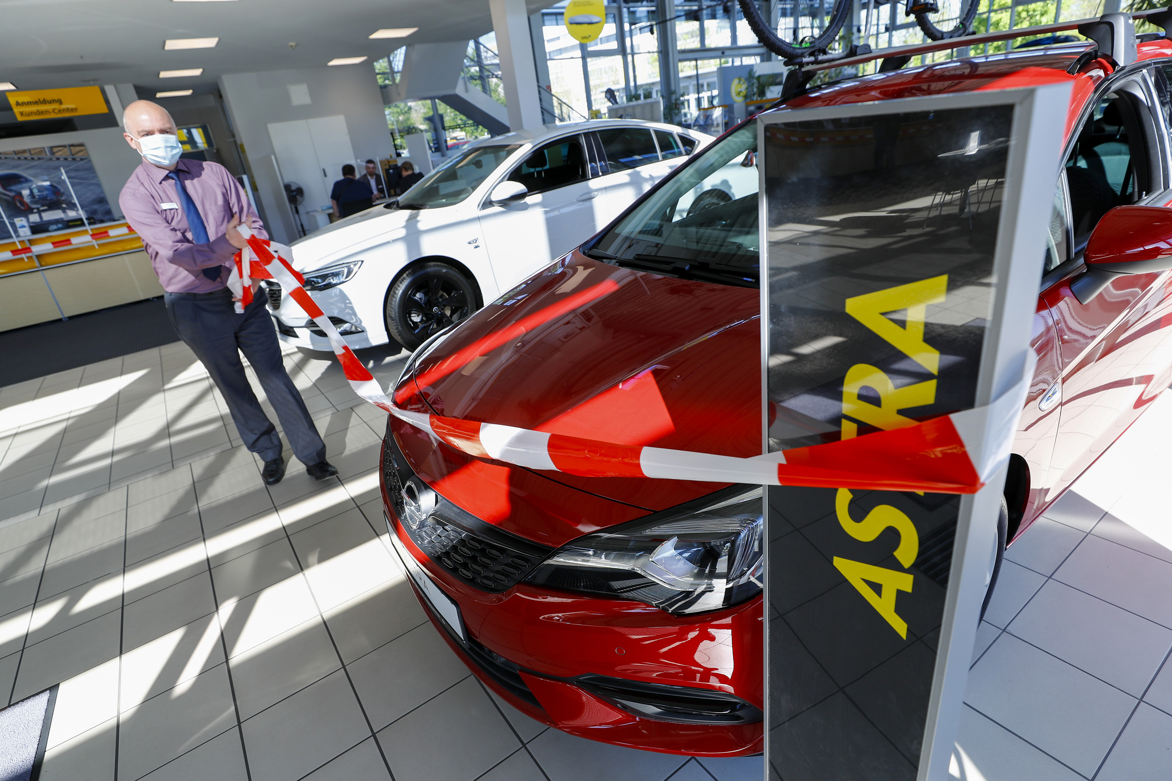 An employee wearing a protective face mask removes a cordon next to an Opel Astra at a showroom in Ruesselsheim, Germany, on Monday, April 20, 2020. Germany shut businesses and factories over the past month, but a government scheme to pay a portion of wages kept layoffs to a minimum. Wire photography: Alex Kraus—Bloomberg via Getty Images