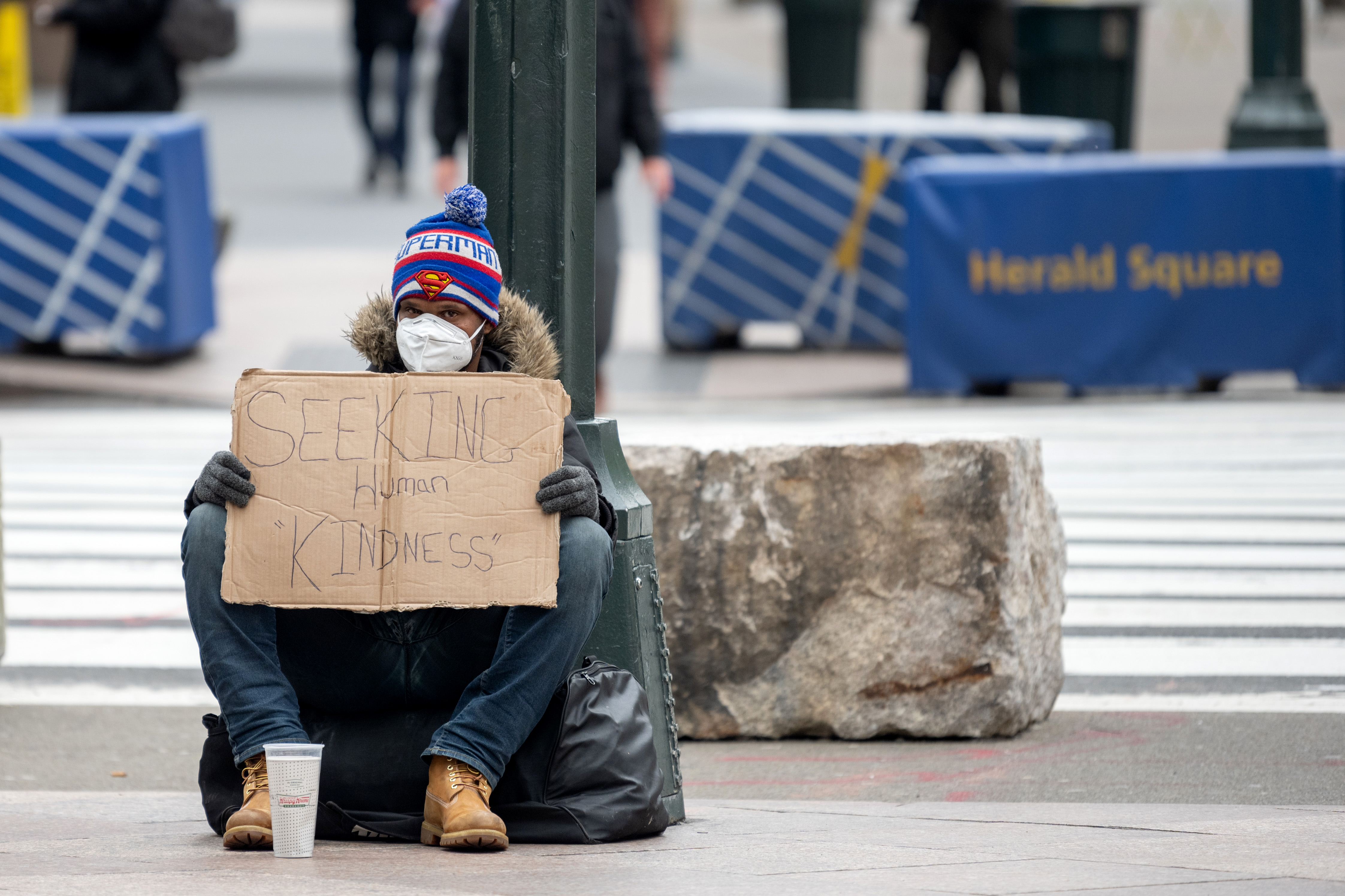 A person wearing gloves and a protective mask sits with a sign that reads, "Seeking Human Kindness" amid the coronavirus pandemic on April 19, 2020 in New York City, United States. A new report out on Thursday expects to push the number of newly unemployed to more than 25 million. Wire photography: Alexi Rosenfeld—Getty Images