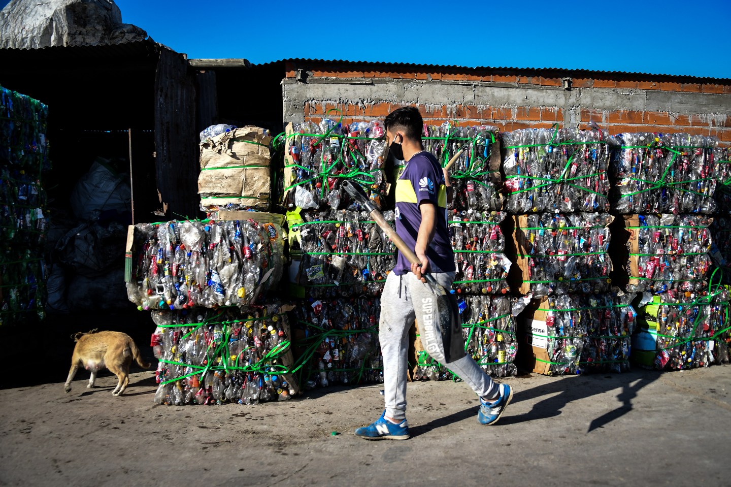 A man wearing a face mask and holding a shovel walks by compacted plastic bottles for recycling at Villa Itati on May 28, 2020 in Quilmes, Argentina.