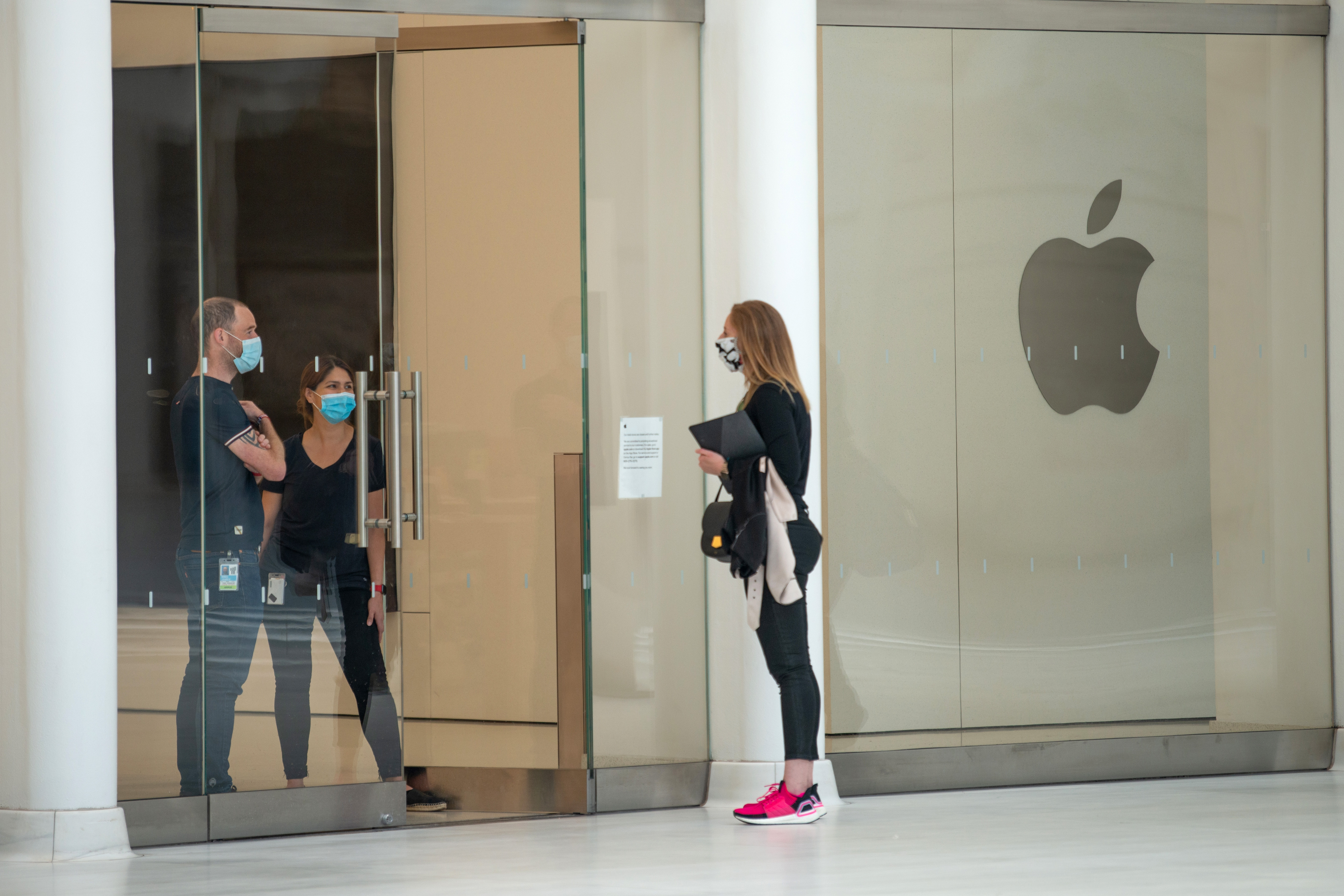Apple store employees wearing masks talk to a customer through an open door.   Alexi Rosenfeld—Getty Images