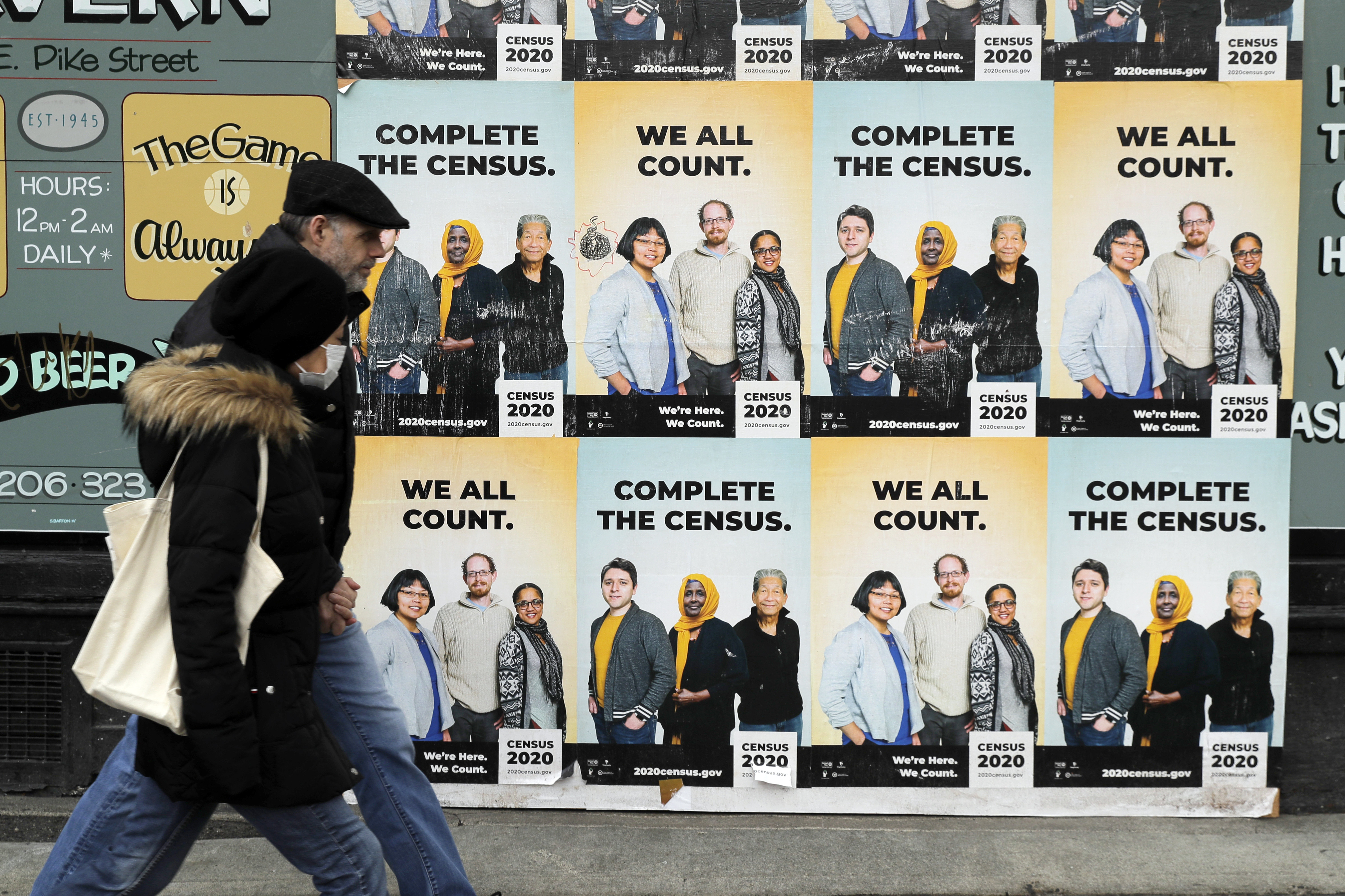 In this April 1, 2020, photo, people walk past posters encouraging participation in the 2020 Census in Seattle's Capitol Hill neighborhood. Just how badly has the new coronavirus impacted life in the U.S.? The U.S. Census Bureau, along with five other federal agencies, will try to answer that question with a new experimental, weekly survey that just got approved earlier this week. Ted S. Warren—AP Photo