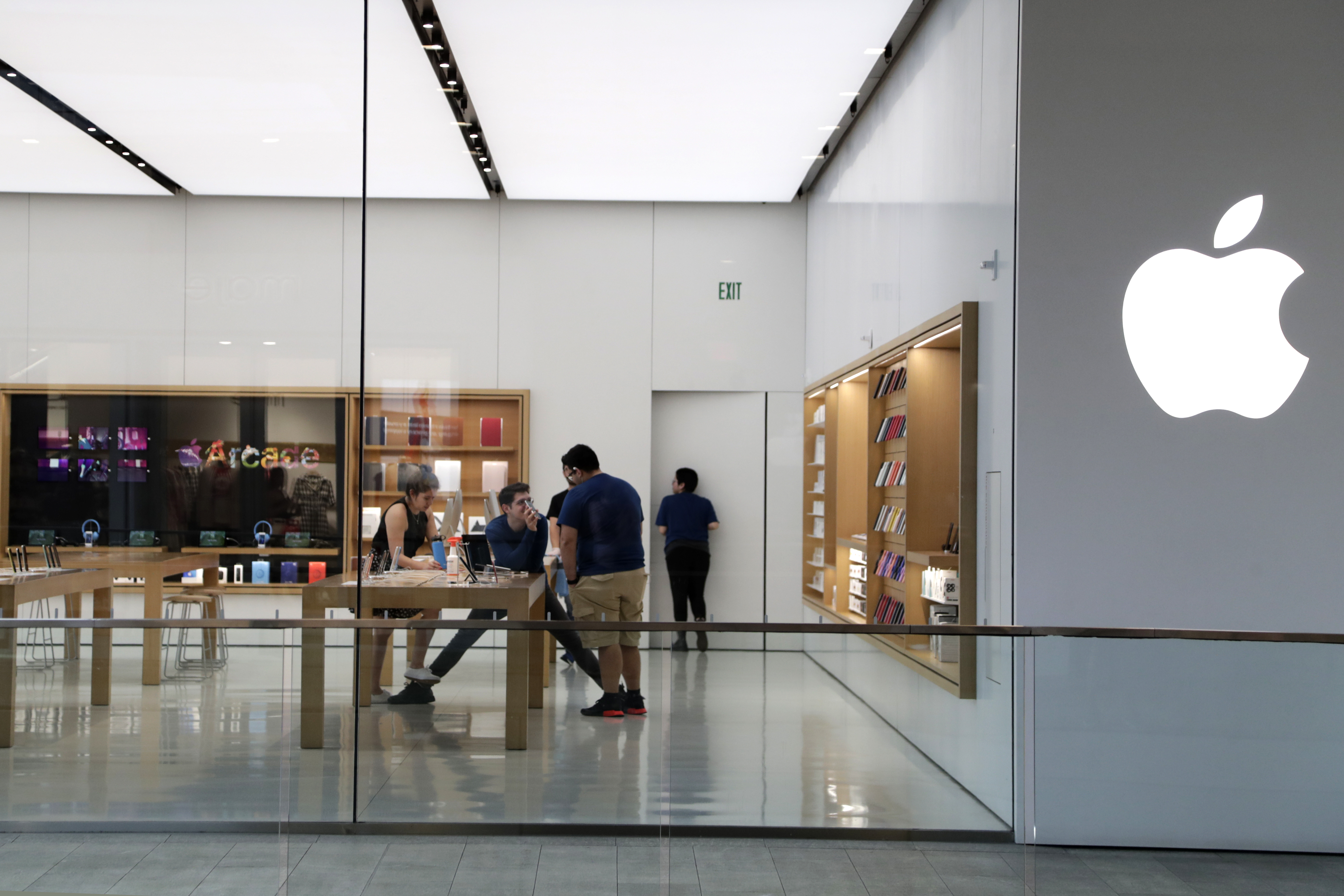 In this March 14 2020 photo, Apple employees work inside a closed Apple store in Miami. Apple is temporarily closing 11 stores in Arizona, Florida, North Carolina and South Carolina just few weeks after reopening them in hopes that consumers would be able to shop in them without raising the risk of infecting them or company workers with the novel coronavirus that caused COVID-19.