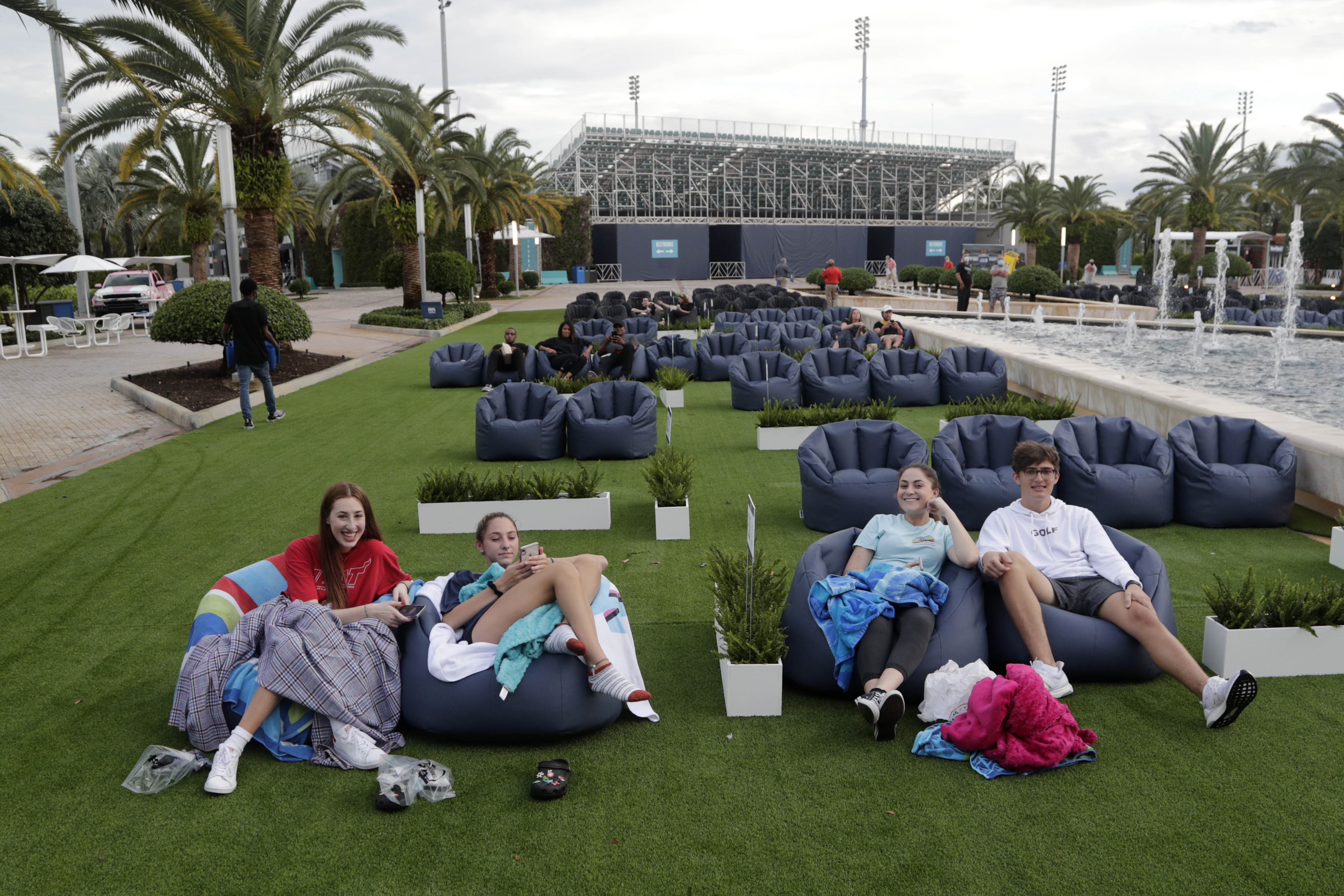 In this Thursday, June 18, 2020 file photo, people sit outdoors to watch a movie as part of a program offered by the Miami Dolphins at Hard Rock Stadium during the coronavirus pandemic in Miami Gardens, Fla. Elected officials such as Florida's governor have argued against reimposing restrictions, saying many of the newly infected are young and otherwise healthy. But younger people, too, face the possibility of severe infection and death. And authorities worry that older, more vulnerable people could be next. 
