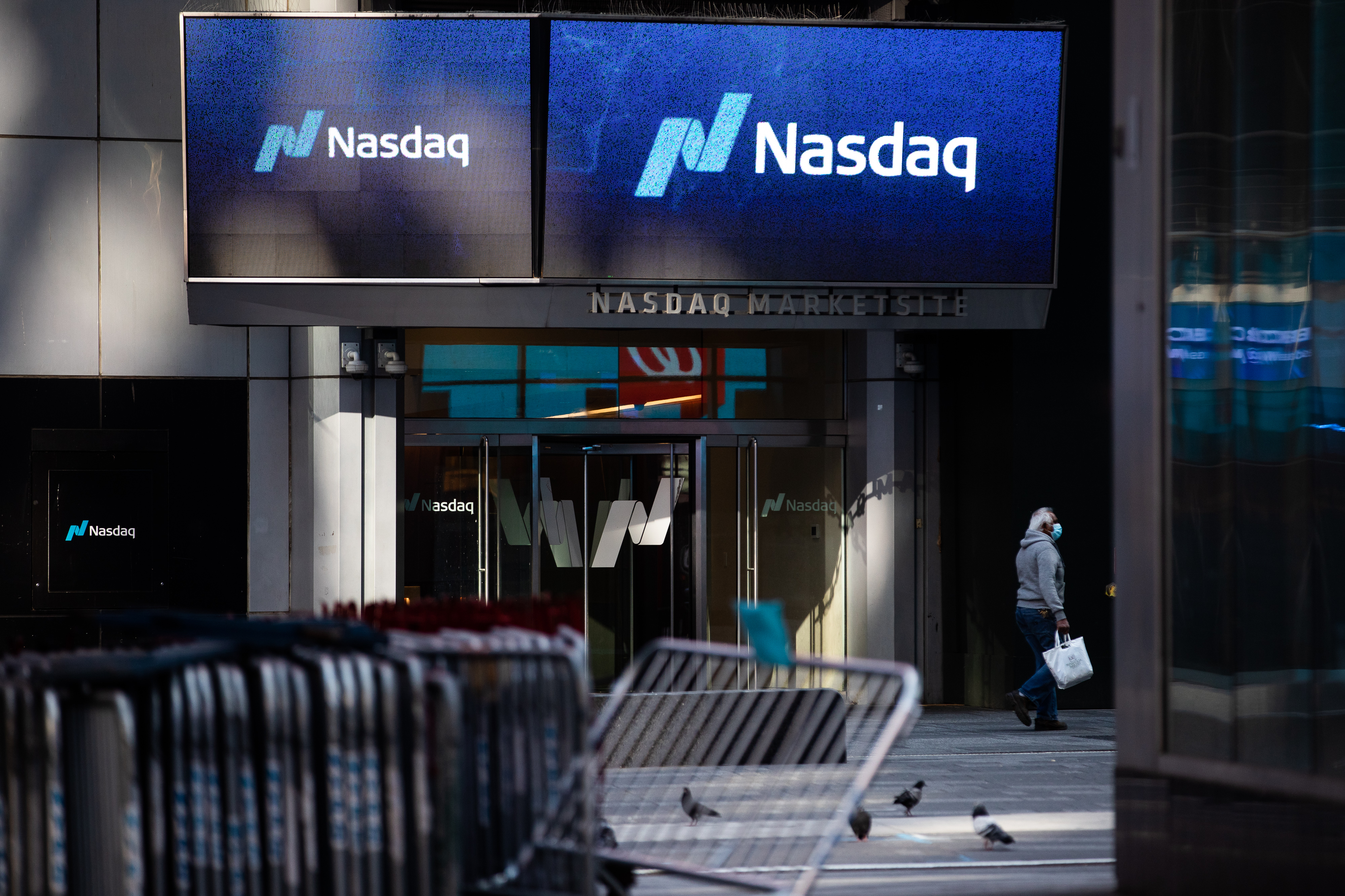 A pedestrian wearing a protective mask passes in front of the Nasdaq Market Site in the Times Square area of New York. The tech-heavy index is poised to open higher to extend its longest rally of the year. Wire photography: Demetrius Freeman—Bloomberg via Getty Images