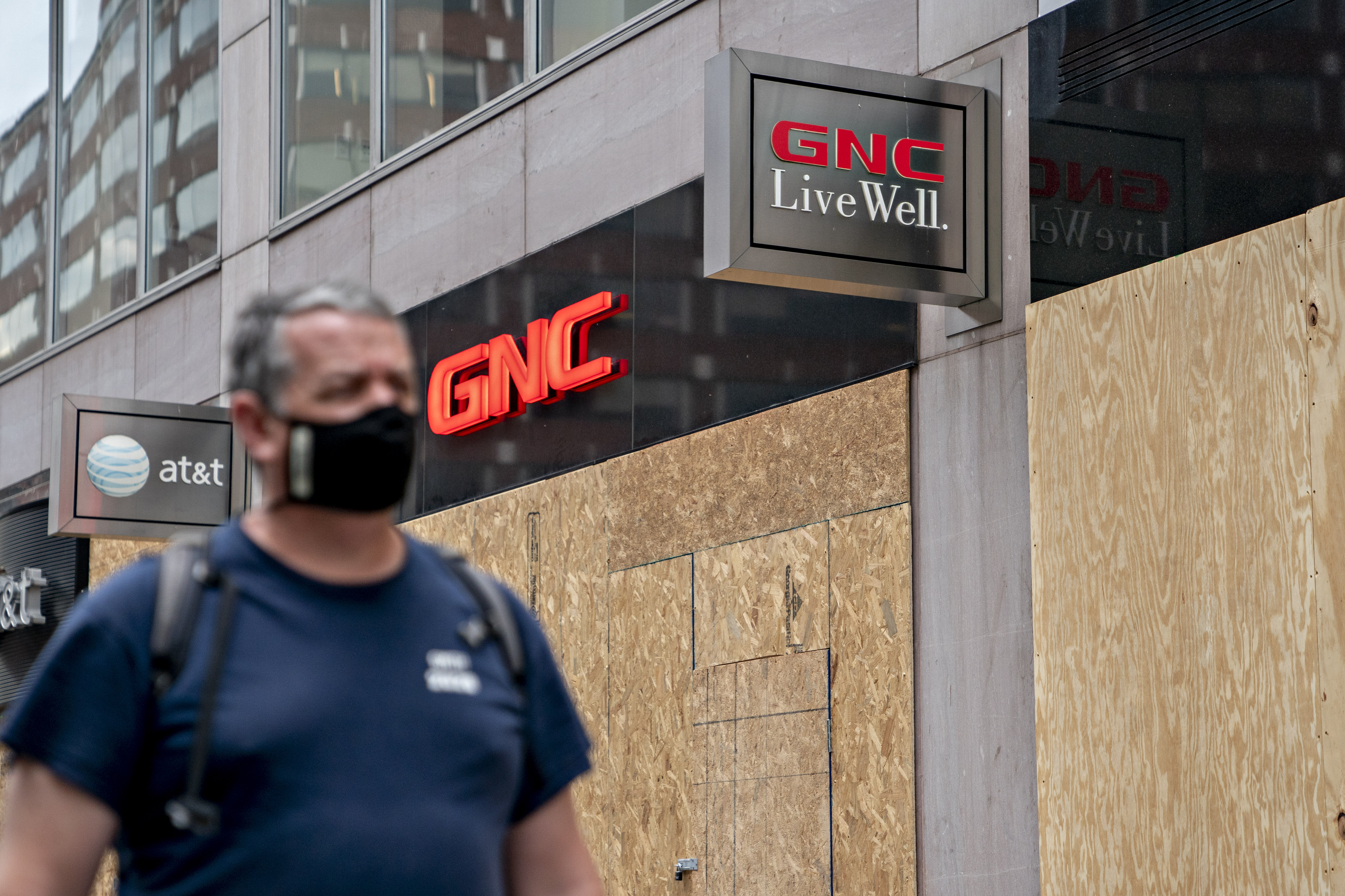 A pedestrian wearing a protective mask walks past a boarded-up GNC store in Washington, D.C., on June 4, 2020. GNC Holdings Inc. and its senior lenders are negotiating a bankruptcy loan just days before a crucial debt deadline for the vitamin retailer, according to people with knowledge of the matter. Photographer: Andrew Harrer/Bloomberg via Getty Images