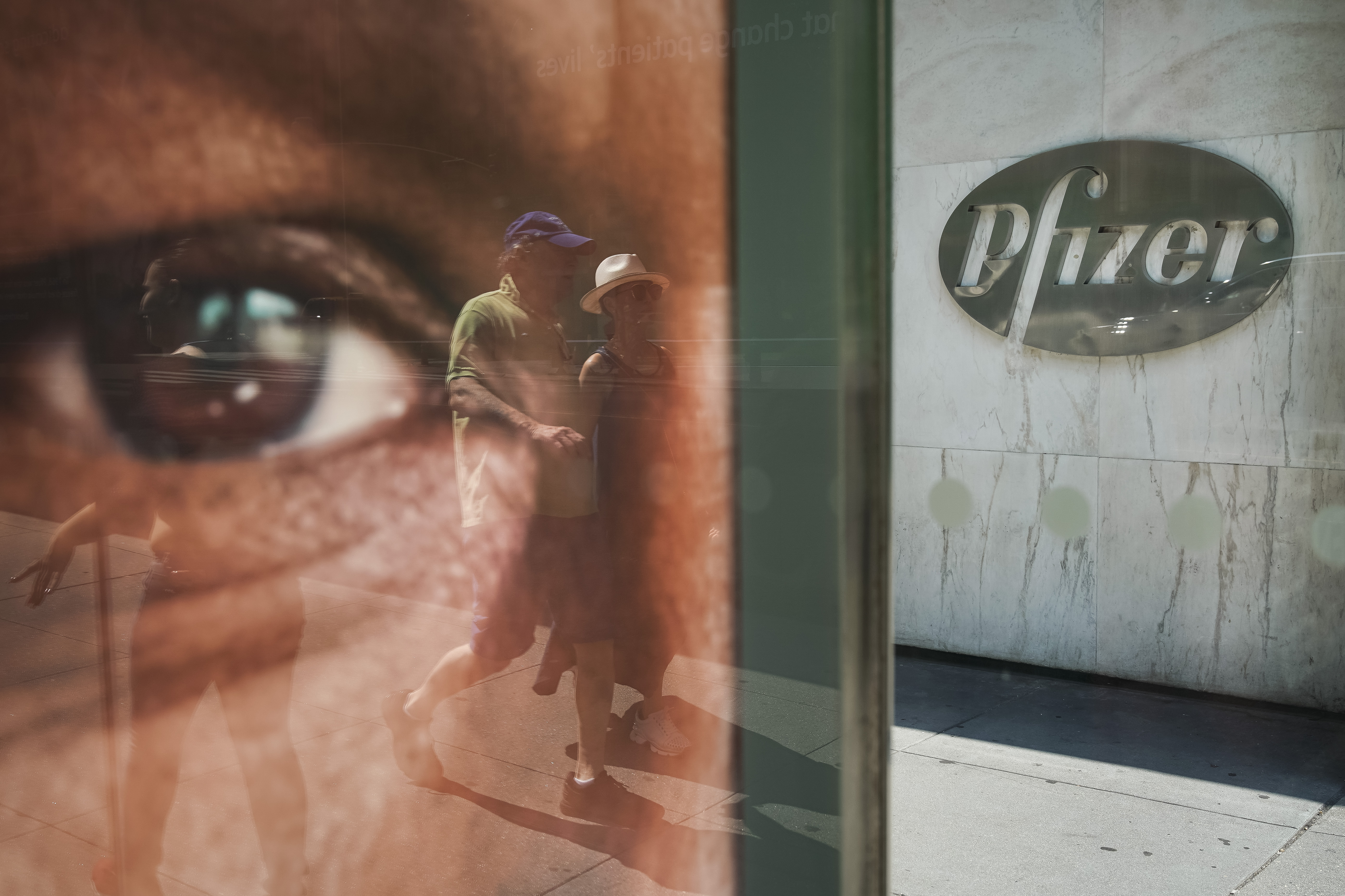 NEW YORK, NY - JULY 29: People are reflected in a bus stop window as they walk past the Pfizer world headquarters in Midtown Manhattan on July 29, 2019 in New York City. On Monday morning, Pfizer announced the merger of its off-patent drug business with generic drugmaker Mylan. The new combined company will be based in the United States and Mylans EpiPen and Pfizers Viagra will be among its portfolio of products. (Photo by Drew Angerer/Getty Images)