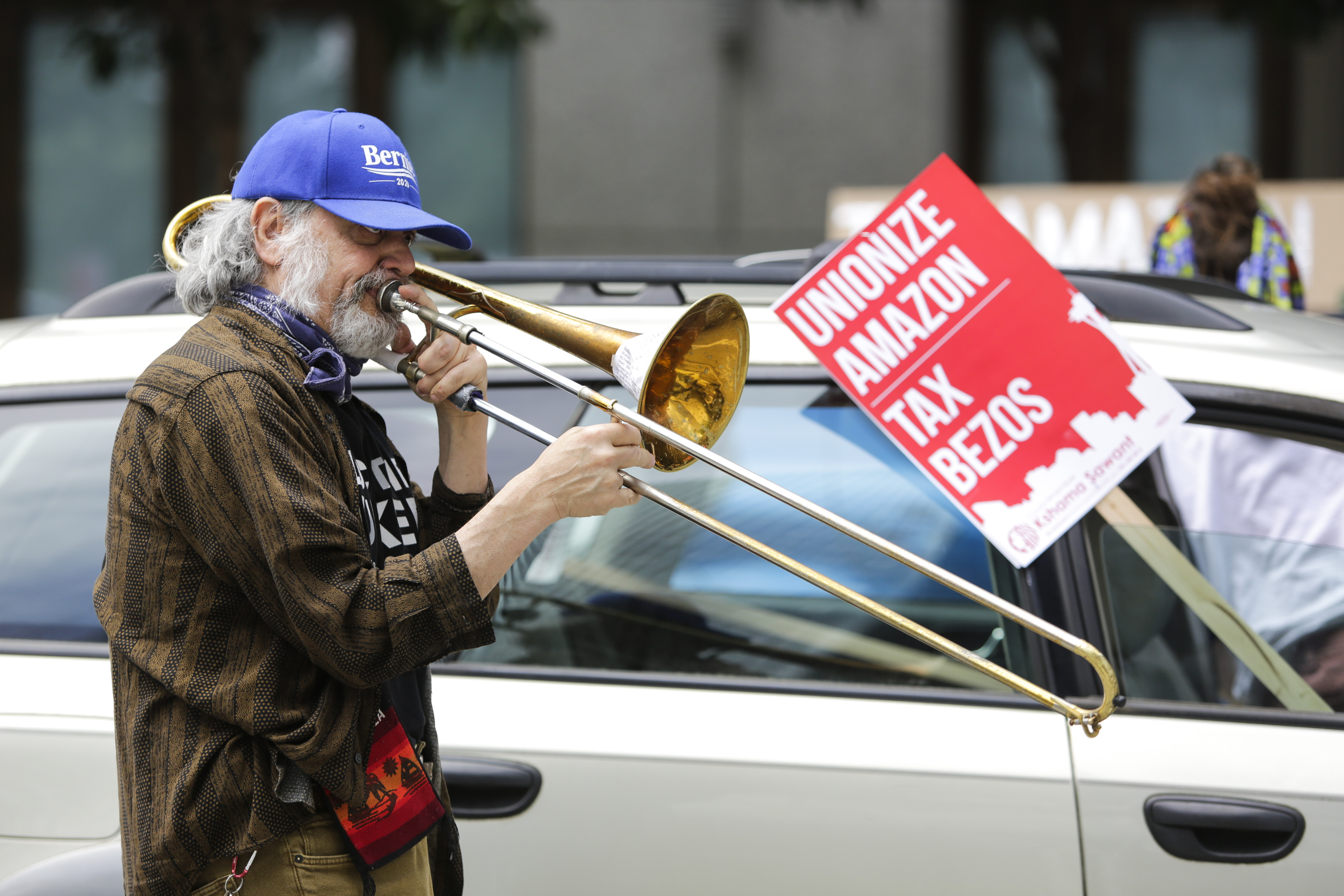 A protester plays a trombone as vehicles circle the block during a "car caravan" protest at the Amazon Spheres to demand the Seattle City Council tax the city's largest businesses in Seattle, Washington on May 1, 2020. - U.S. employees of Amazon, its supermarket subsidiary Whole Foods and supermarket delivery services were called to strike on May 1, taking advantage of May 1 to denounce employers accused of not sufficiently protecting them in the face of the pandemic. (Photo by Jason Redmond / AFP) (Photo by JASON REDMOND/AFP via Getty Images)