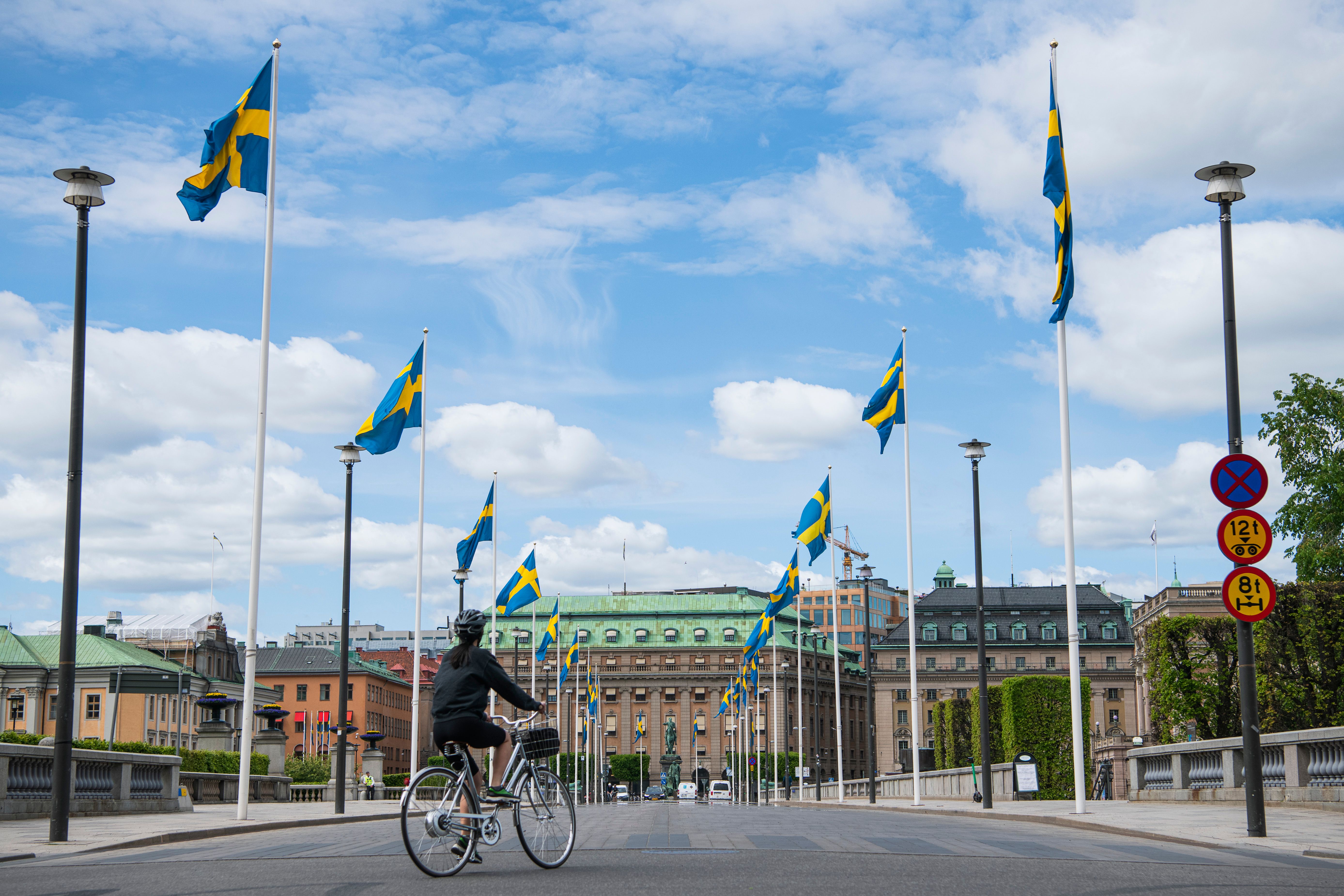 Swedish flags fly as a woman rides her bike in Stockholm on May 29, 2020, amid the coronavirus COVID-19 pandemic. - Sweden's two biggest opposition parties called Friday for an independent commission to be appointed within weeks to probe the country's response to the new coronavirus. (Photo by Jonathan NACKSTRAND / AFP) (Photo by JONATHAN NACKSTRAND/AFP via Getty Images)