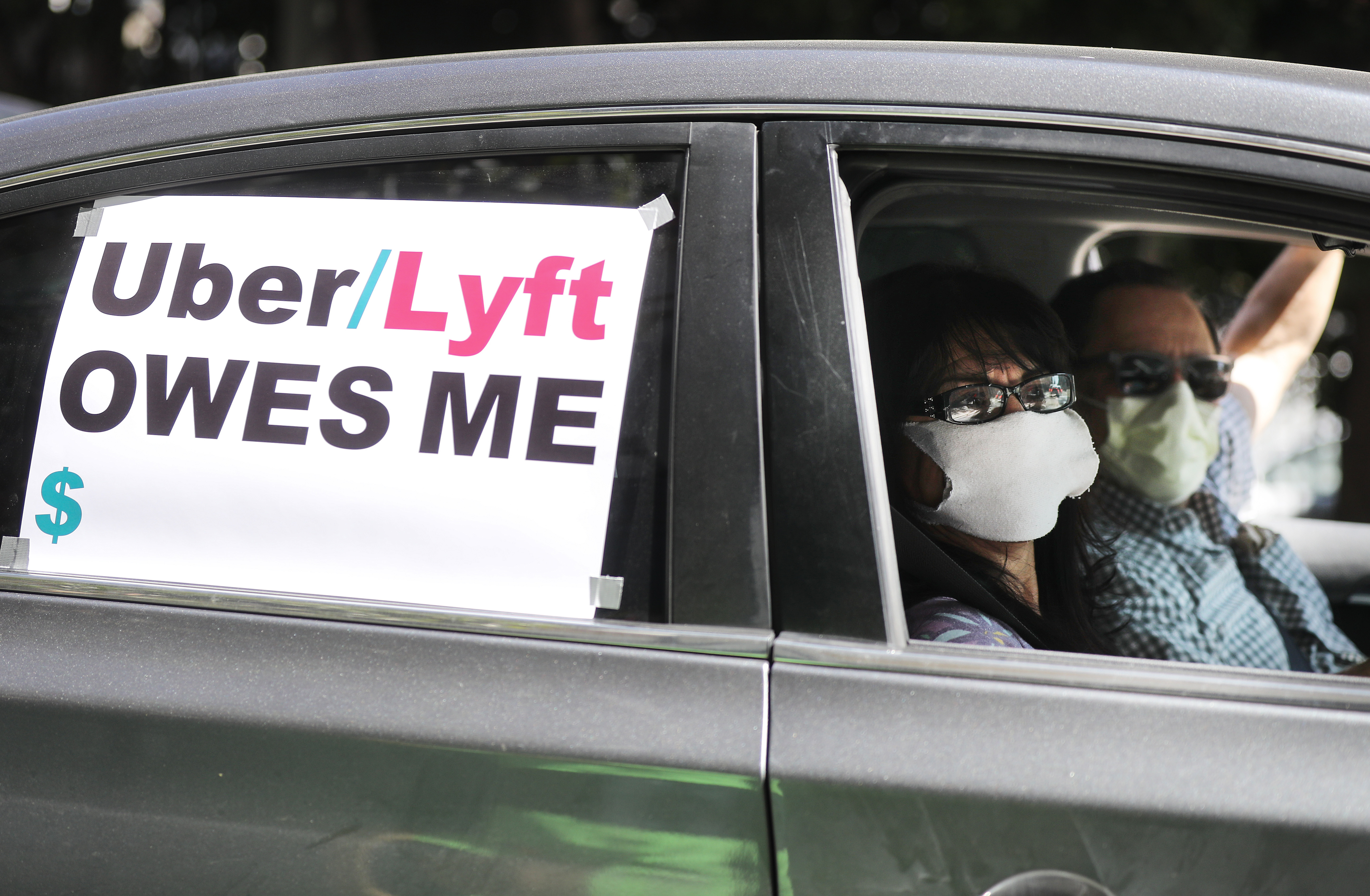 LOS ANGELES, CALIFORNIA - APRIL 16: A driver and passenger wear face masks as Uber and Lyft drivers with Rideshare Drivers United and the
Transport Workers Union of America conduct a ‘caravan protest’ outside the California Labor Commissioner’s office amidst the coronavirus pandemic on April 16, 2020 in Los Angeles, California. The drivers called for California to enforce the AB 5 law so that they may qualify for unemployment insurance as the spread of COVID-19 continues. Drivers also called for receiving back wages they say they are owed. (Photo by Mario Tama/Getty Images)