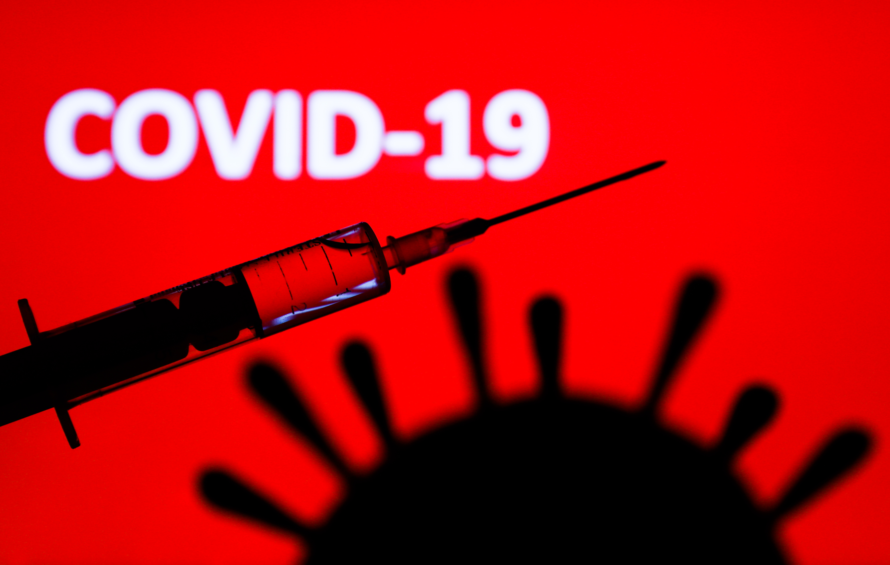Coronavirus model and medical syringe are seen with 'covid-19' sign displayed on a screen in the background in this illustration photo taken in Poland on June 9, 2020. American biotech company Moderna has announced on June 11 that will start final stage of covid-19 vaccine trial in July. (Photo Illustration by Jakub Porzycki/NurPhoto via Getty Images)