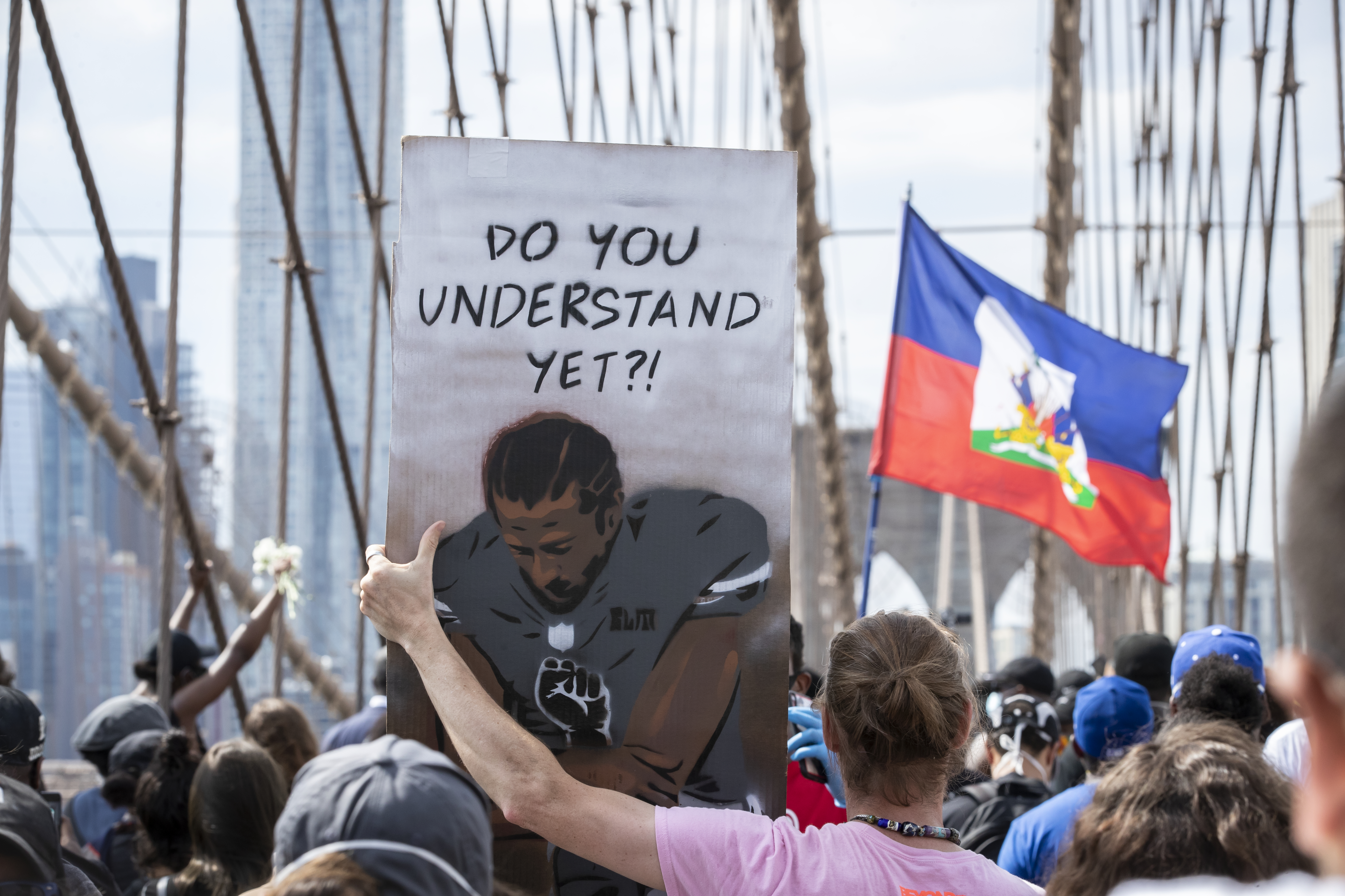 A protester holds a sign that says,"Do You Understand Yet?" with a picture of Colin Kaepernick, former quarterback for the San Francisco 49ers, taking a knee with a Black Power Fist on in the middle of his jersey with the Arches of the Brooklyn Bridge behind them as they walk across the Brooklyn Bridge in protest of police racism. Protesters walked from Brooklyn to Manhattan after a memorial ceremony in Brooklyn with Terrence Floyd, brother of George Floyd. Protesters have taken to the streets across America and around the world after the killing of George Floyd at the hands of a white police officer Derek Chauvin that was kneeling on his neck during his arrest as he pleaded that he couldn't breathe. Ira L. Black—Corbis via Getty Images