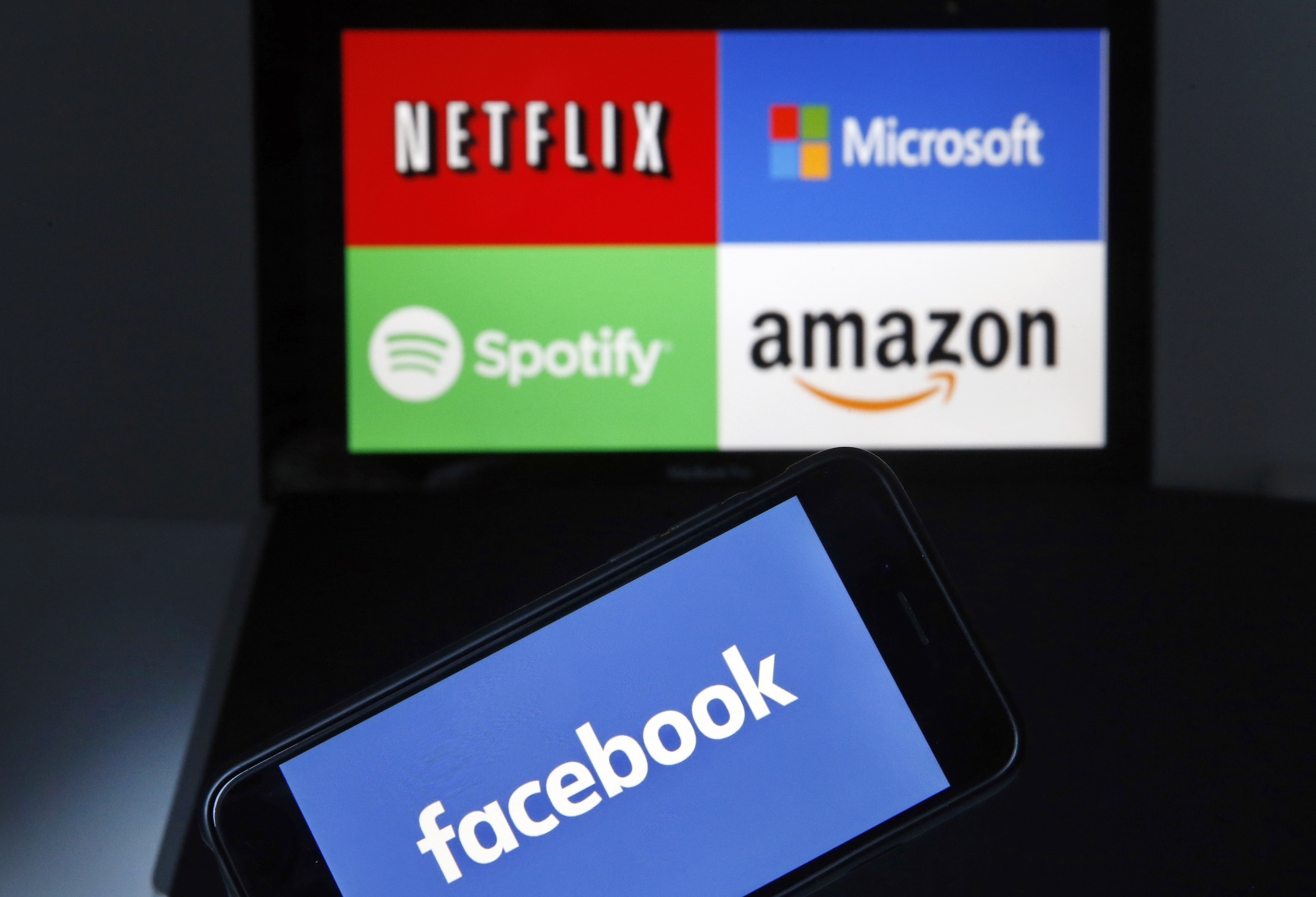 PARIS, FRANCE - DECEMBER 20: In this photo illustration the Facebook logo is seen on the screen of an iPhone in front of a computer screen showing Amazon, Netflix, Spotify and Microsoft logos on December 20, 2018 in Paris, France. The social network Facebook has authorized giants like Amazon, Netflix, Spotify and Microsoft to access the personal data of its 2.2 billion users according to the "New York Times". Facebook has granted broad access to these companies because of their privileged status, a practice that would constitute an offense. Washington's Attorney General, Karl Racine, has just launched a lawsuit against Facebook. (Photo by Chesnot/Getty Images)