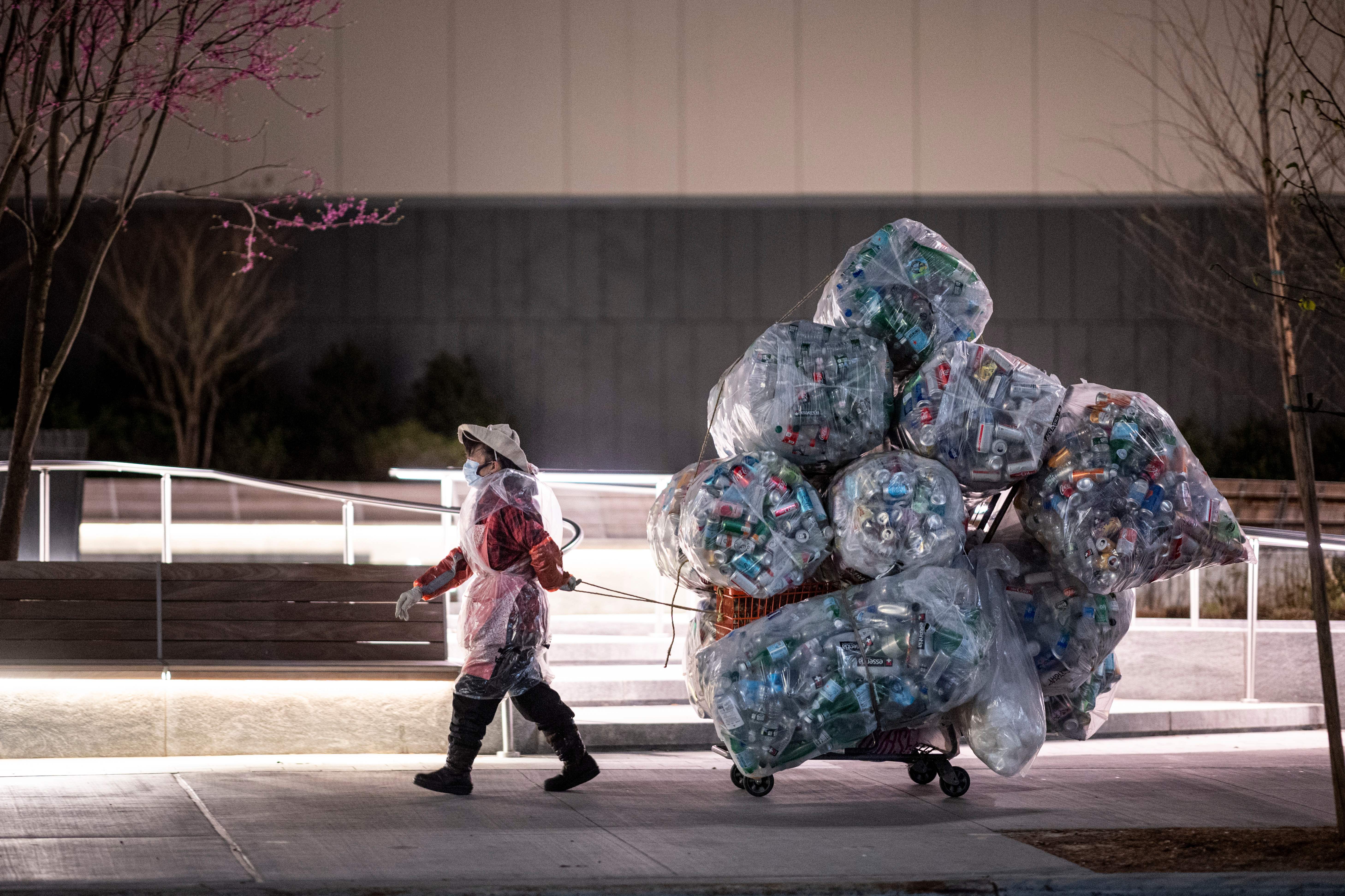 TOPSHOT - A woman wearing a face mask and a plastic bag pulls a cart loaded with bags of recyclables through the streets of Lower Manhattan during the outbreak of the novel coronavirus (which causes COVID-19) on April 16, 2020 in New York City. (Photo by Johannes EISELE / AFP) (Photo by JOHANNES EISELE/AFP via Getty Images)