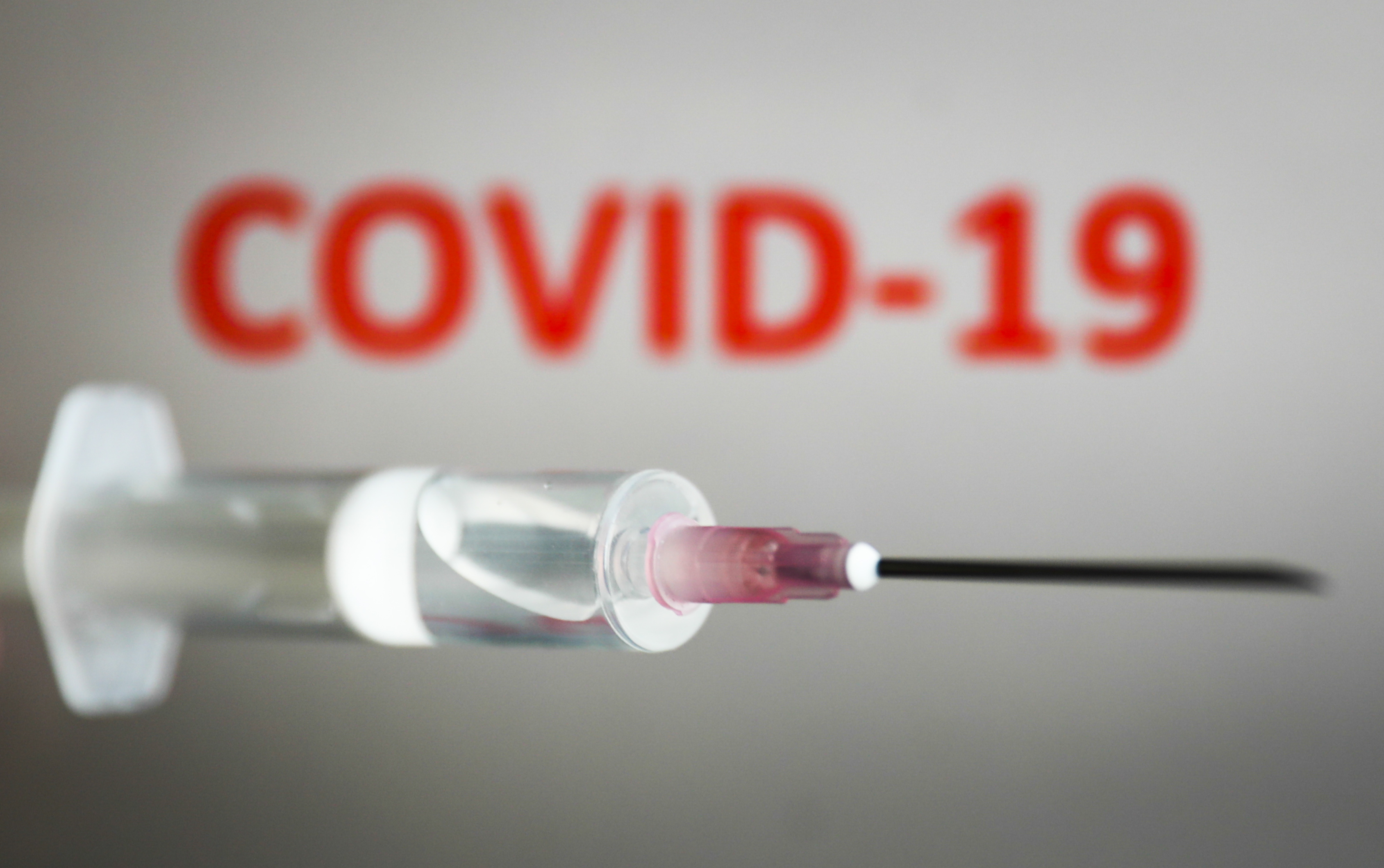 Medical syringe is seen with 'covid-19' sign displayed on a screen in the background in this illustration photo taken in Poland on July 20, 2020. Early trial of the coronavirus vaccine developed by the Oxford University showed that it is safe and triggers an immune response. (Photo Illustration by Jakub Porzycki/NurPhoto via Getty Images)