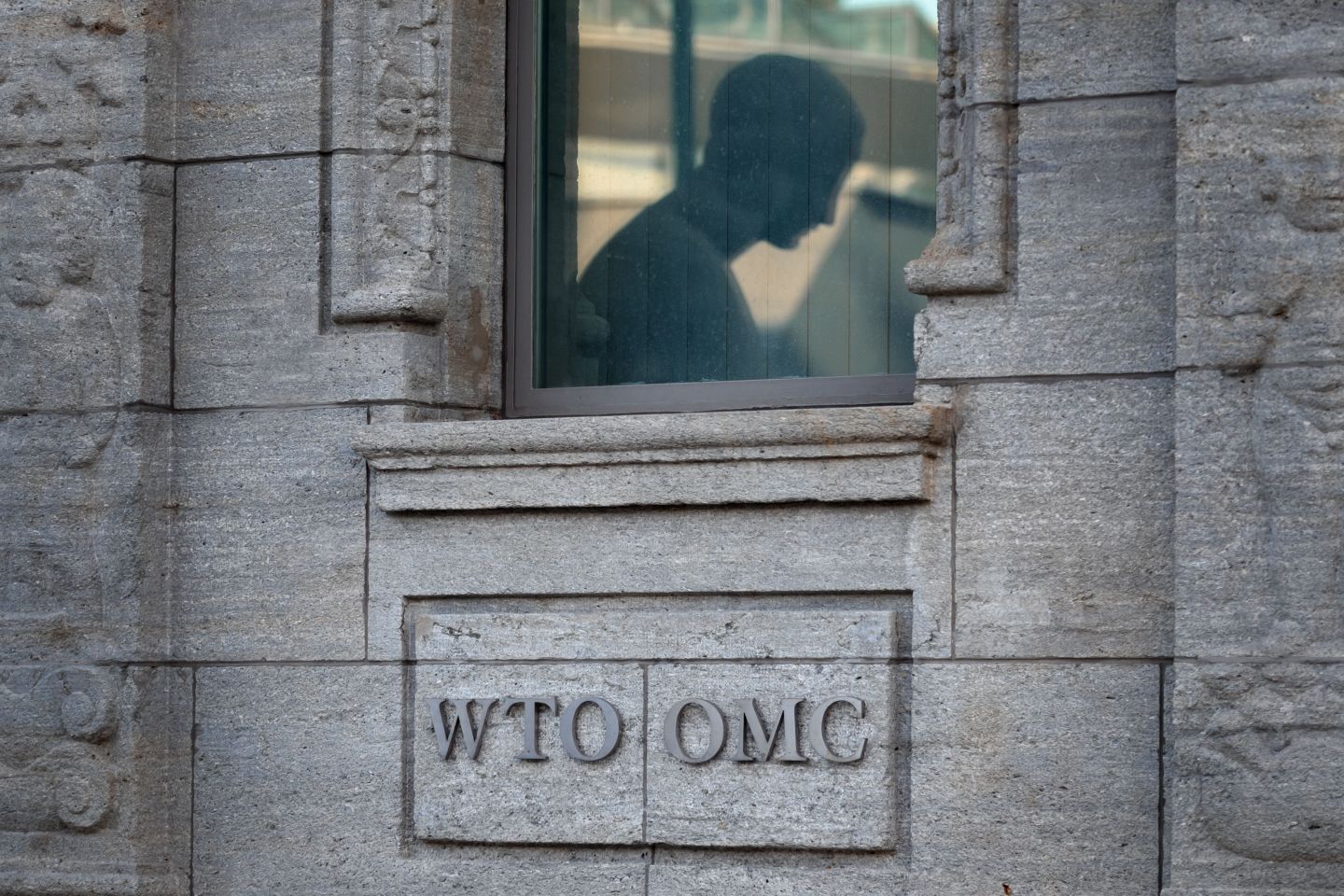 A picture taken on July 23, 2020 shows the silhouette of a statue reflected in a window above a sign at the entrance of the World Trade Organization (WTO) prior to a general council in Geneva.