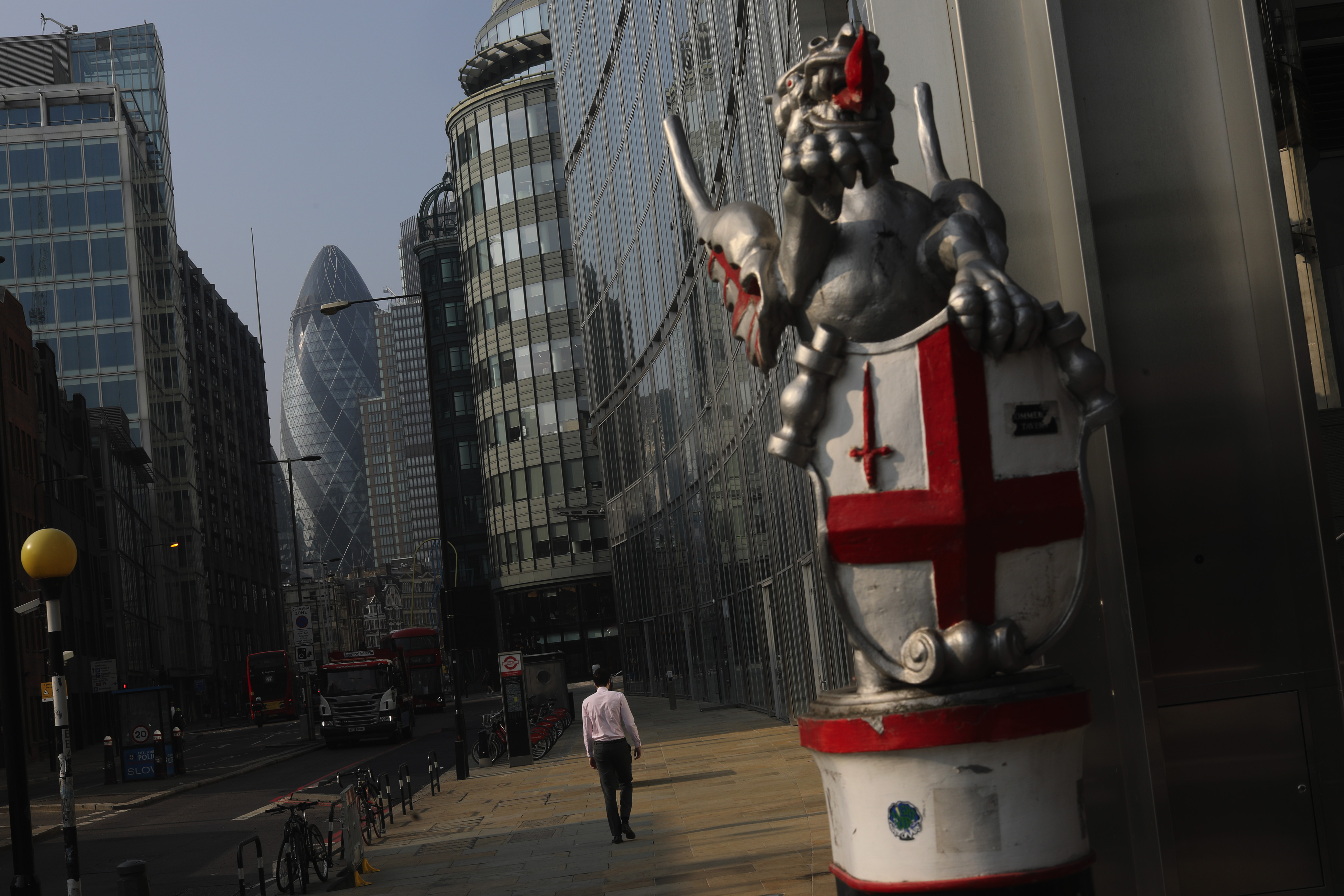 A city worker passes a 'City of London Dragon' statue near skyscrapers including 30 St. Mary's Axe, also known as the Gherkin, center, in London, U.K., on Wednesday, Aug. 12, 2020. The pandemic hit the U.K. hardest in Europe with the countrys economy contracting more than 20% in the second quarter. Photographer: Simon Dawson/Bloomberg via Getty Images