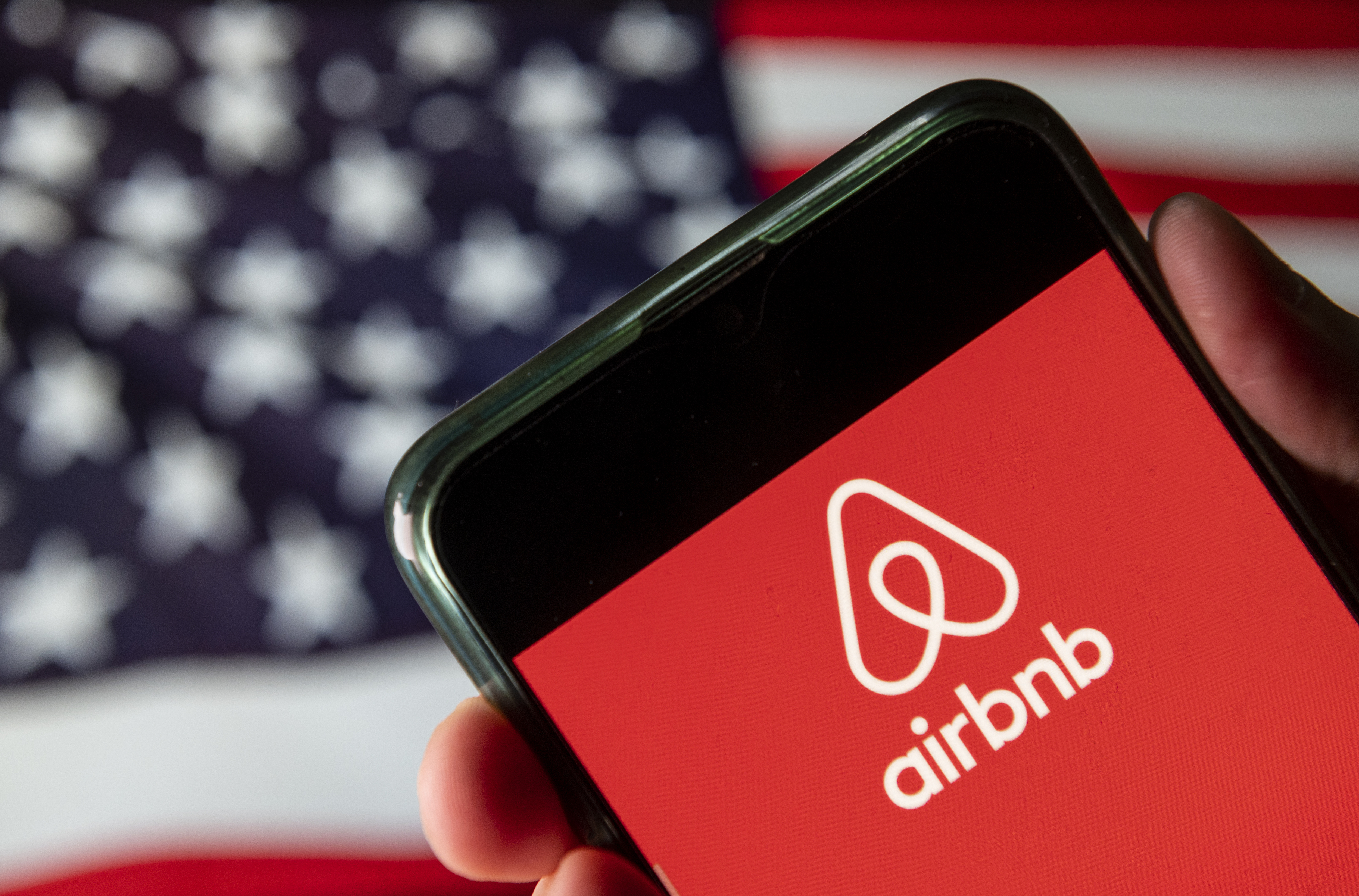 CHINA - 2020/08/15: In this photo illustration the American online marketplace and hospitality service Airbnb logo is seen on an Android mobile device with United States of America flag in the background.