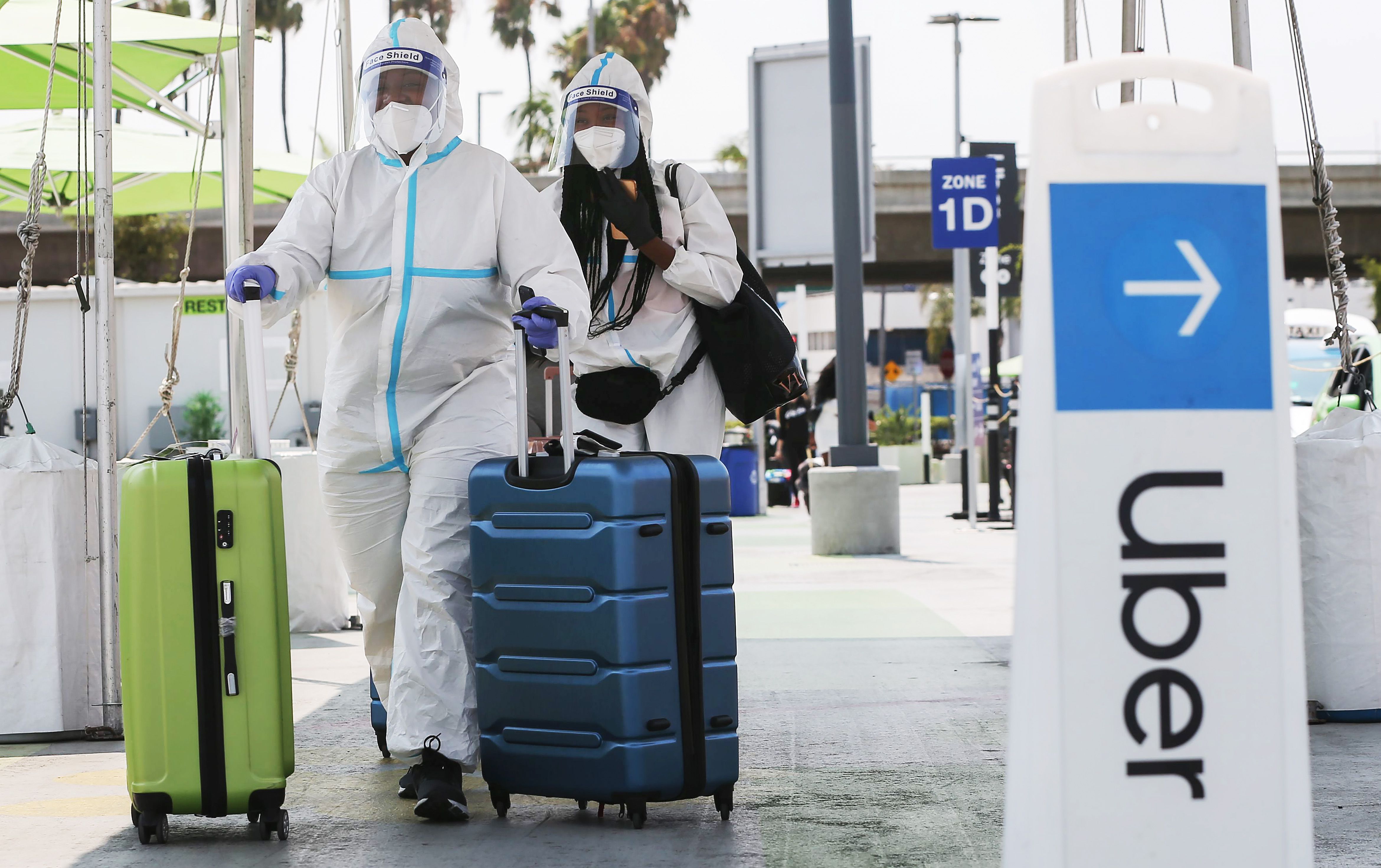 LOS ANGELES, CALIFORNIA - AUGUST 20: Air travelers arriving from New York in personal protective equipment (PPE) walk past an Uber sign on their way to board a Lyft vehicle at Los Angeles International Airport (LAX) on August 20, 2020 in Los Angeles, California. Uber and Lyft drivers held a rally earlier at the airport calling for basic employment rights. An appeals court granted Lyft and Uber an emergency stay from needing to classify drivers as employees allowing ride-sharing services to continue after a threatened shutdown in California. (Photo by Mario Tama/Getty Images)