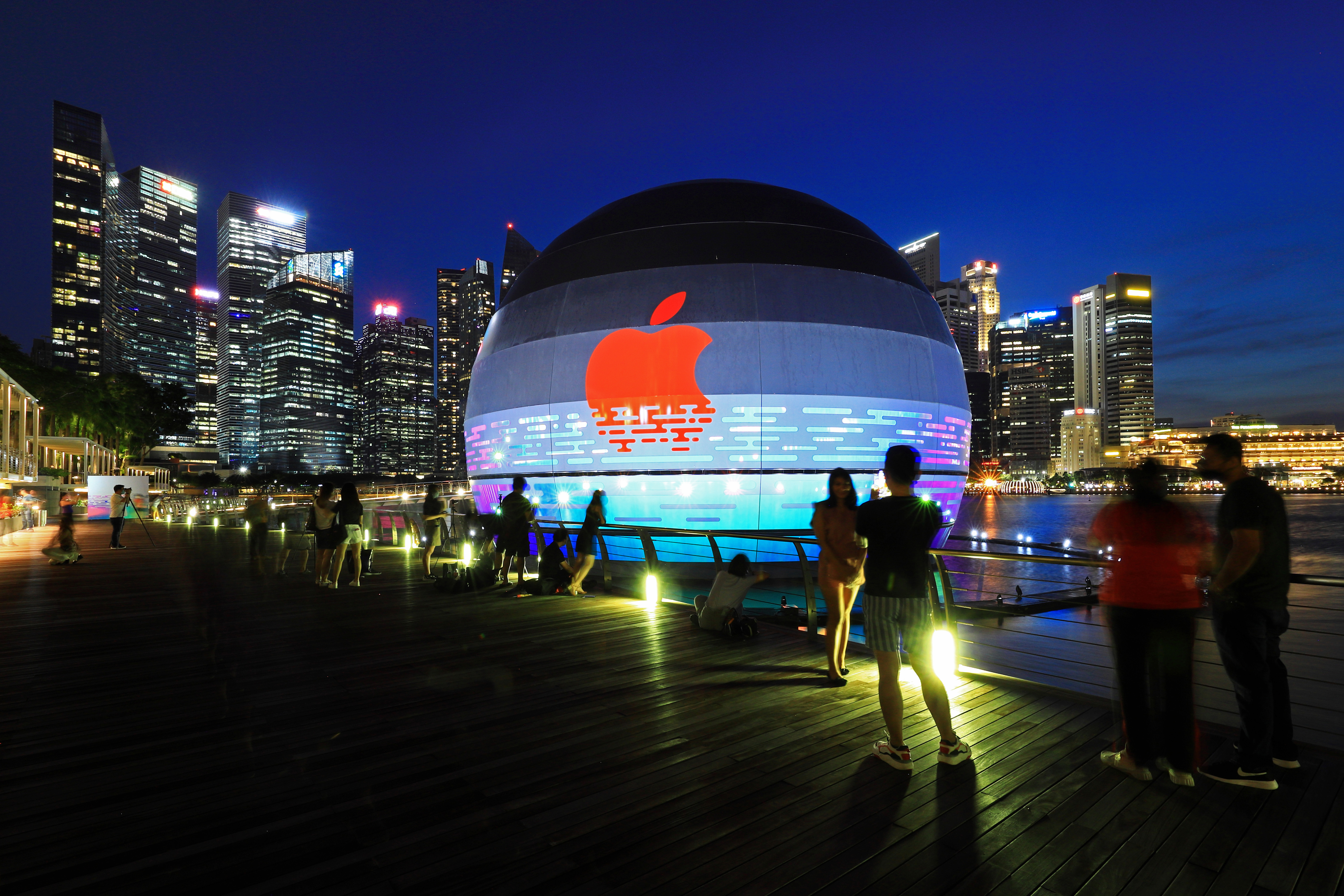 SINGAPORE - AUGUST 28: People take photos of the new Apple flagship store against the city skyline at Marina Bay Sands waterfront on August 28, 2020 in Singapore. The store located in a futuristic giant glass orb is the third Apple store to open in Singapore.