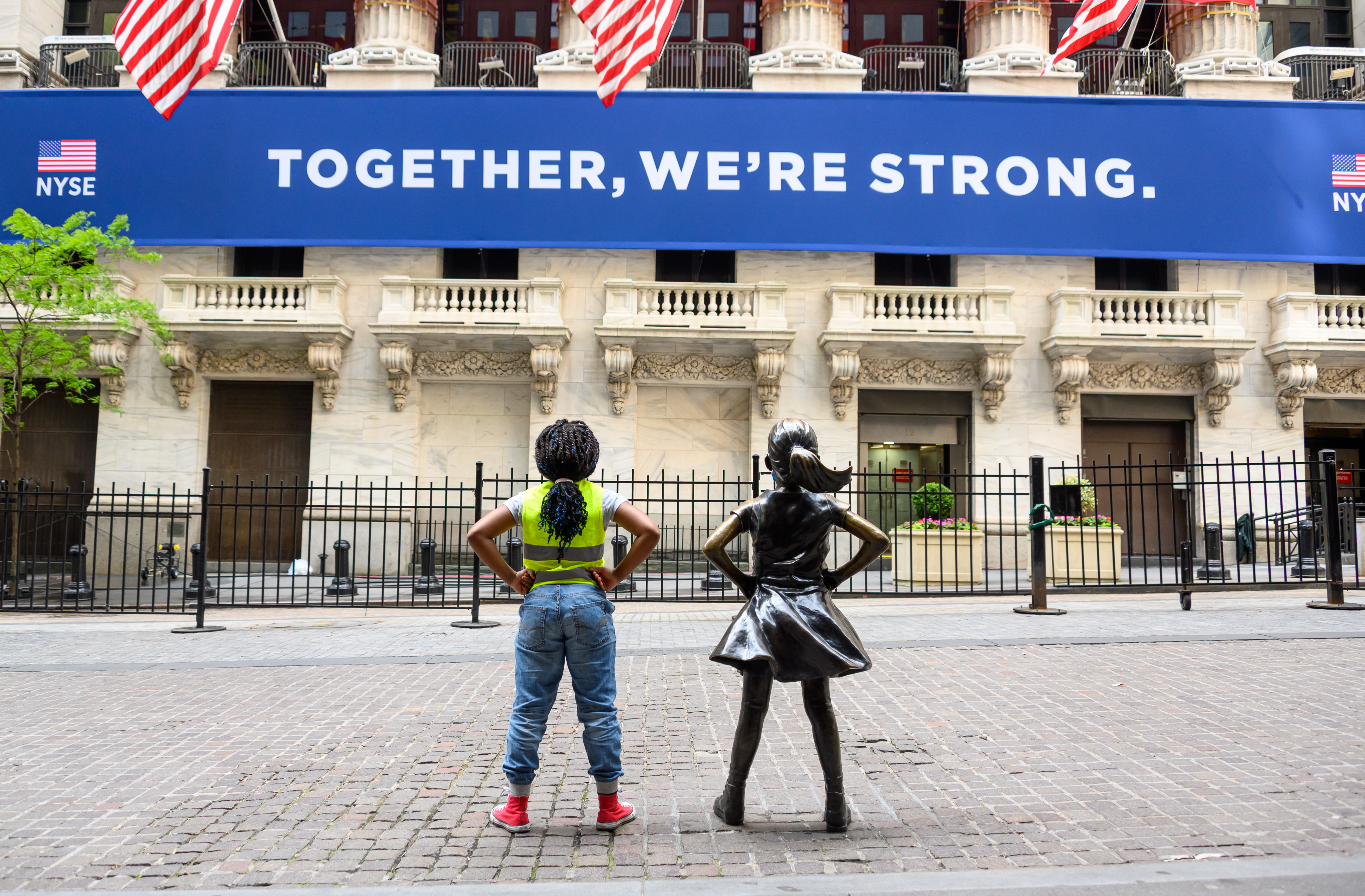 NEW YORK, NEW YORK - MAY 25: A kid poses next to the Fearless Girl statue outside the New York Stock Exchange during the coronavirus pandemic on May 25, 2020 in New York City. Government guidelines encourage wearing a mask in public with strong social distancing in effect as all 50 states in the USA have begun a gradual process to slowly reopen after weeks of stay-at-home measures to slow the spread of COVID-19. (Photo by Noam Galai/Getty Images)