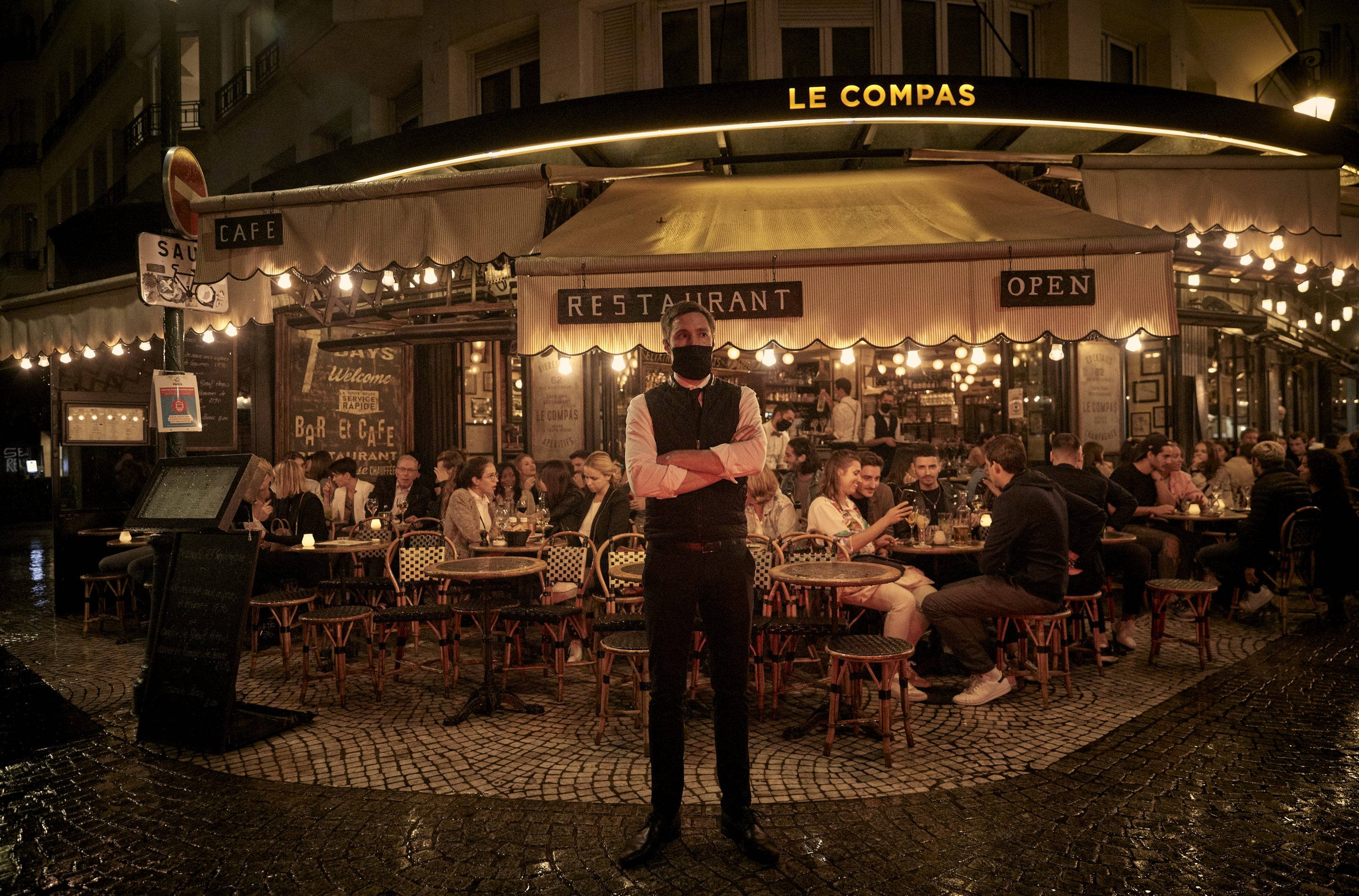 PARIS, FRANCE - SEPTEMBER 23: A waiter stands outside a busy terrace as Parisians relax as the French Government announced that from Monday all bars and cafes in Paris will be made to shut at 10pm as part of a string of new measures to curb the spread of Covid-19 in France on September 23, 2020 in Paris, France. With the rise in Coronavirus cases in France at 204 per 100,000 inhabitants, the French Government have followed other governments in introducing new restrictions aimed at reducing the spread of Covid-19 whilst avoiding another national lockdown. In large cities, including Paris, gatherings will be limited to ten people in public spaces, bars to close at 10 p.m., local and student parties will be prohibited. (Photo by Kiran Ridley/Getty Images)