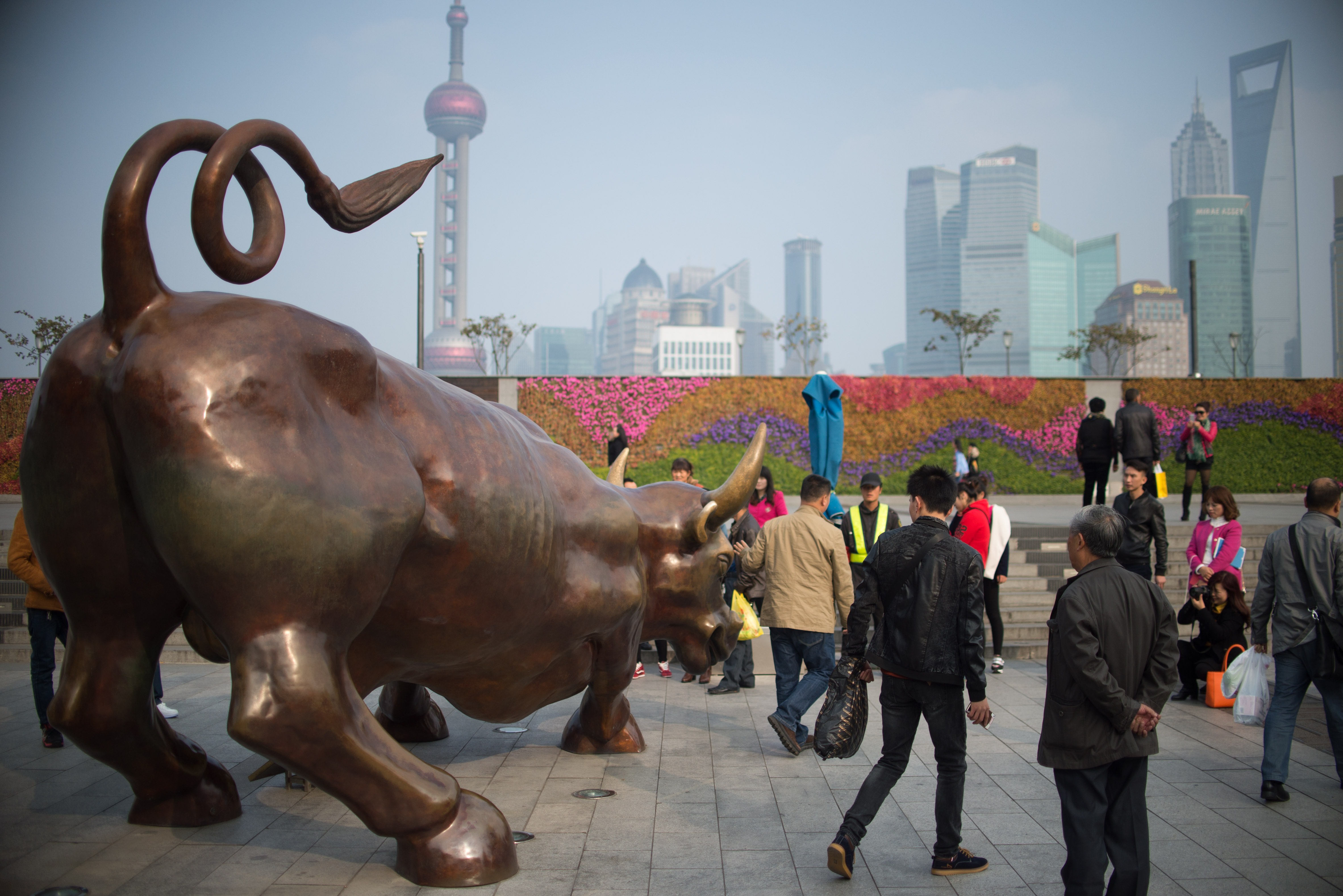 People have photos taken with a replica of the famous Wall Street bronze bull on the Bund in Shanghai on November 17, 2014. The Shanghai-Hong Kong Stock Connect will allow cross trading between two of China's largest financial hubs and will enable international investors to trade selected stocks in Shanghai's tightly restricted exchange and allow mainland traders to buy stocks in Hong Kong.   AFP PHOTO / JOHANNES EISELE        (Photo credit should read JOHANNES EISELE/AFP via Getty Images)