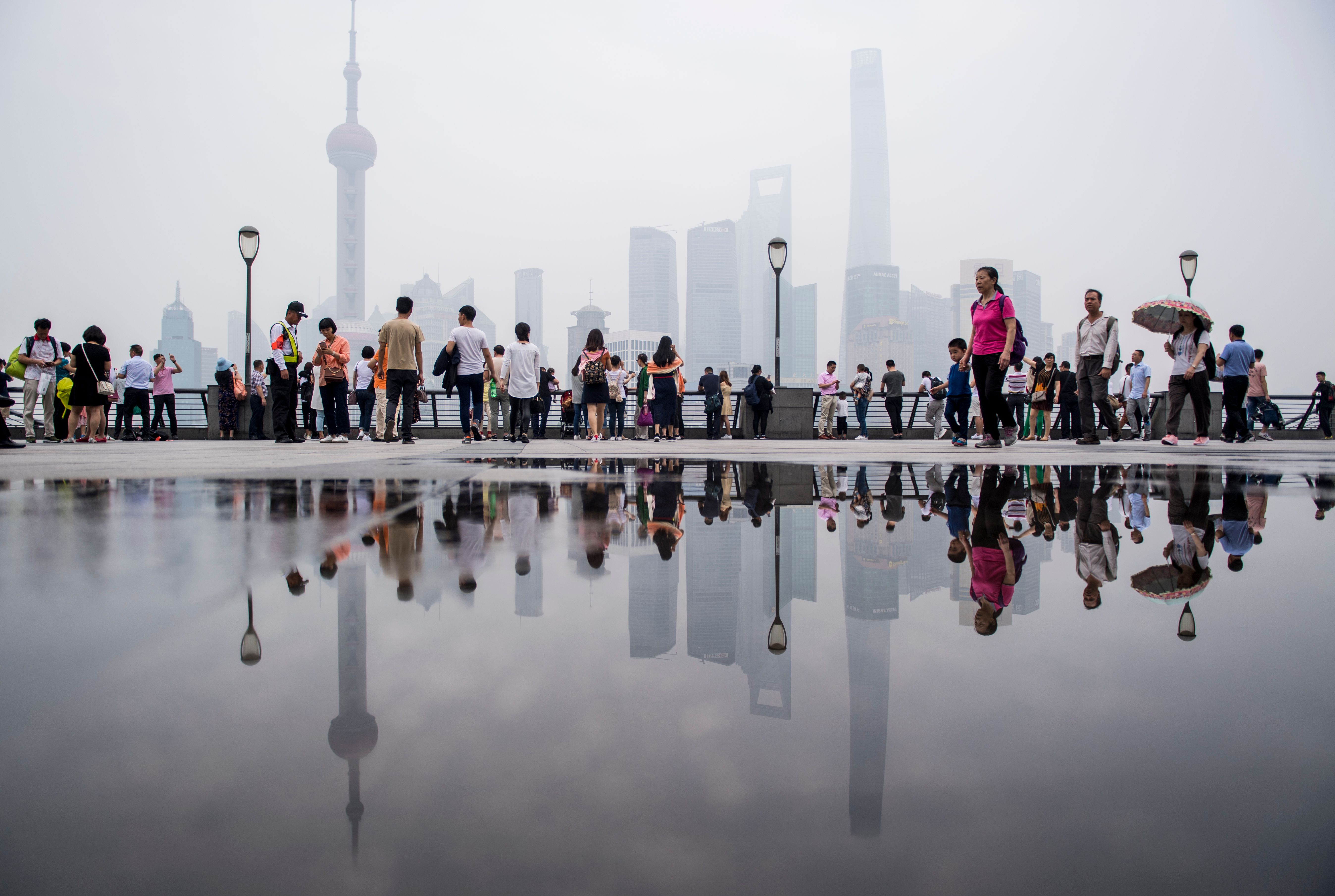 TOPSHOT - Tourists flock to the promenade on the Bund along the Huangpu River, seen against the skyline of the Lujiazui Financial District in Shanghai on a hazy and polluted day on May 29, 2018. (Photo by Johannes EISELE / AFP) (Photo credit should read JOHANNES EISELE/AFP via Getty Images)