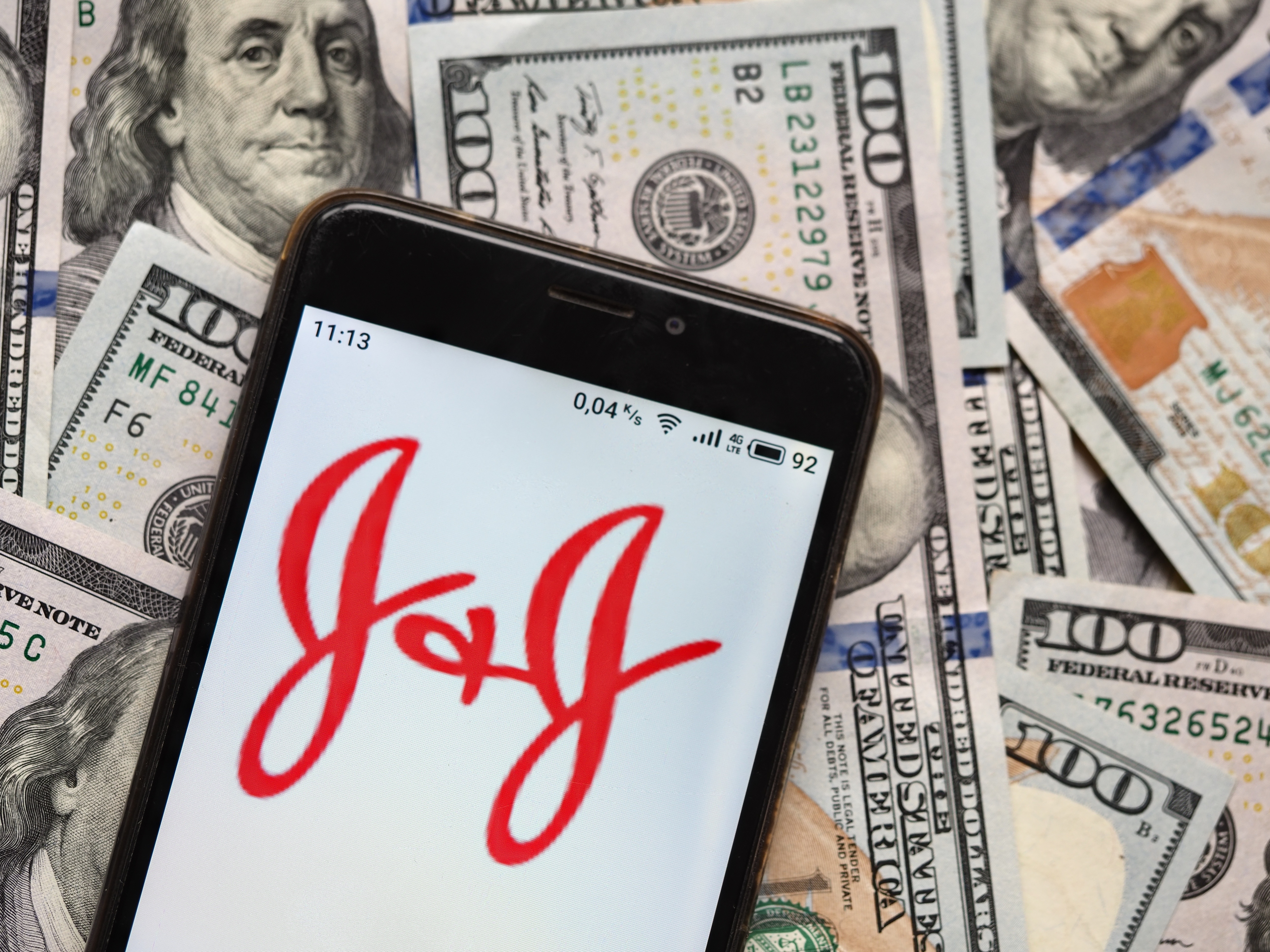 UKRAINE - 2020/09/04: In this photo illustration a Johnson & Johnson logo seen displayed on a smartphone with 100 dollar bills in the background. (Photo Illustration by Igor Golovniov/SOPA Images/LightRocket via Getty Images)