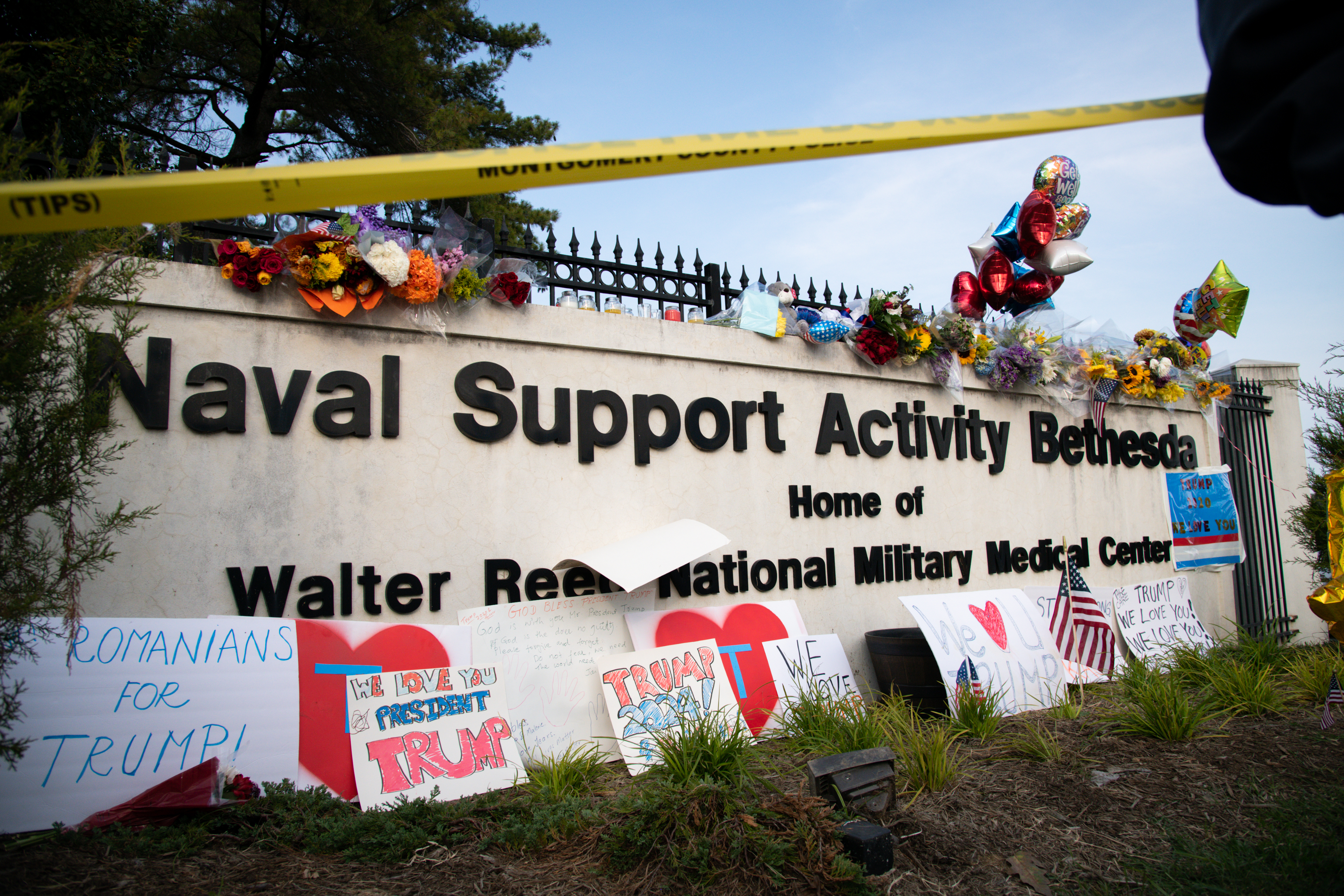 Flowers and signs are displayed as supporters of U.S. President Donald Trump rally outside Walter Reed National Military Medical Center in Bethesda, Maryland, U.S., on Sunday, Oct. 4, 2020. President Donald Trump unexpectedly left the hospital where hes being treated for Covid-19 to greet supporters on Sunday, waving to them from his motorcade in a bid to demonstrate strength while yearning to return to the campaign trail. Photographer: Graeme Sloan/Bloomberg via Getty Images