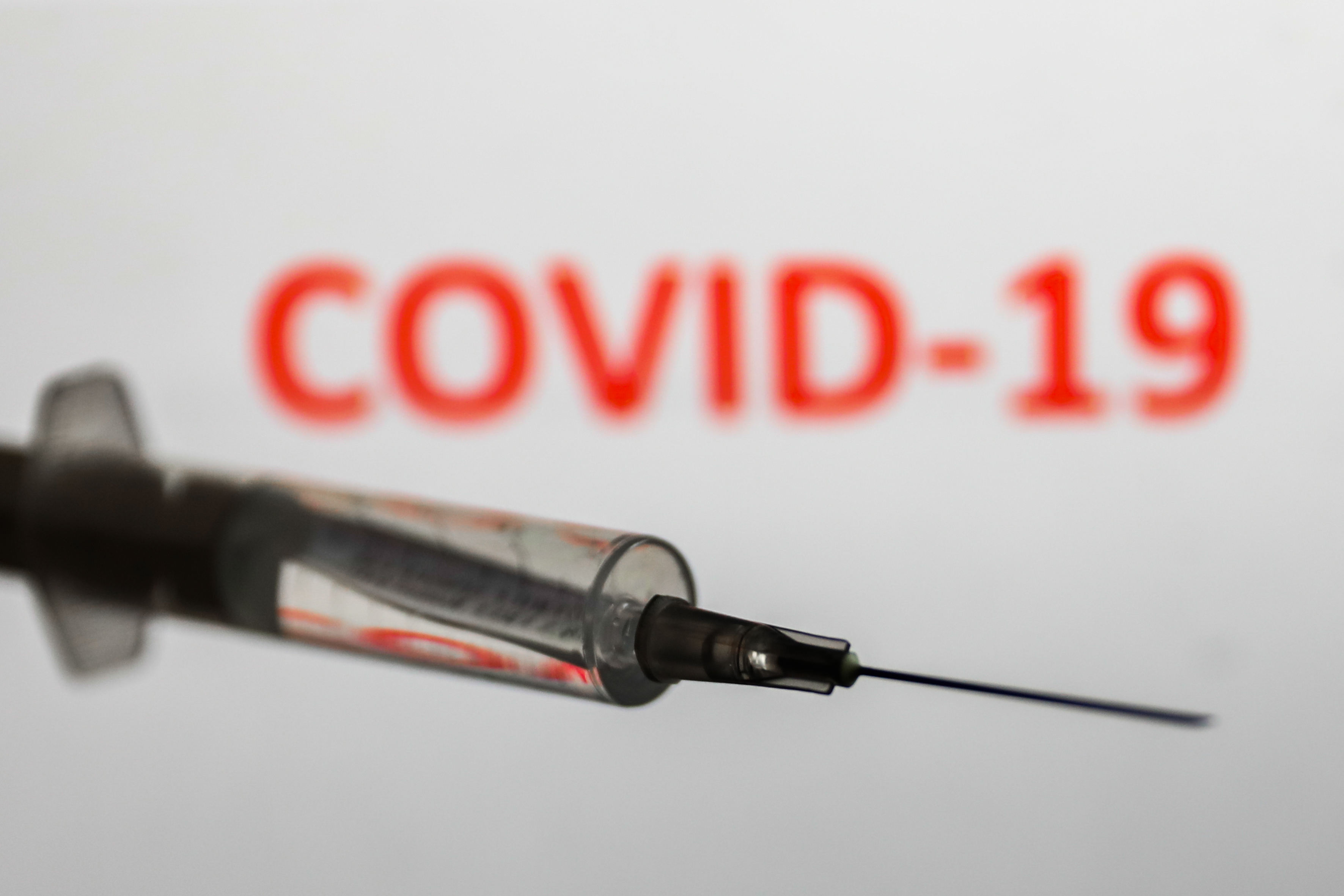 Medical syringe is seen with 'covid-19' sign displayed on a screen in the background in this illustration photo taken in Poland on October 12, 2020.