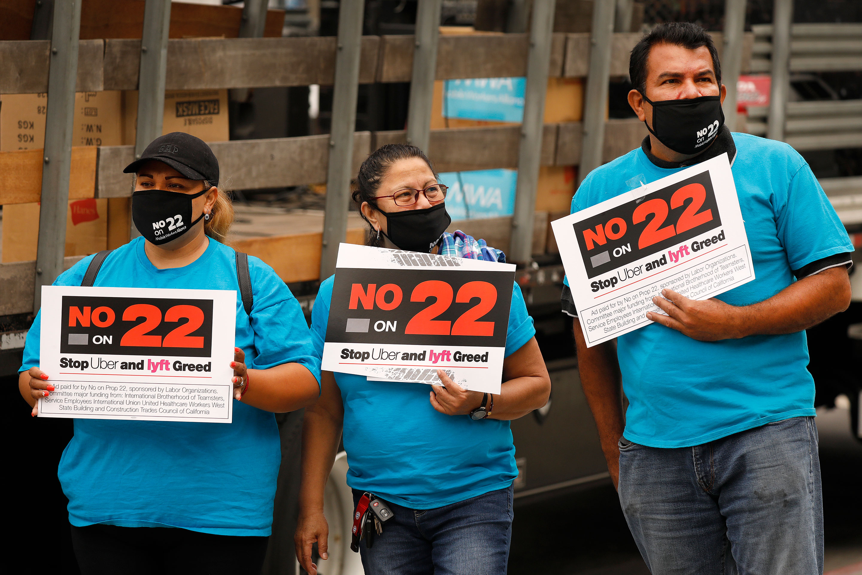 From left: Luz Laguna, Isabelle Ramos, and Leonardo Diaz, with Mobile Workers Alliance, hold signs in front of Los Angeles City Hall, urging voters to vote no on Proposition 22, a November ballot measure that would classify app-based drivers as independent contractors and not as employees.