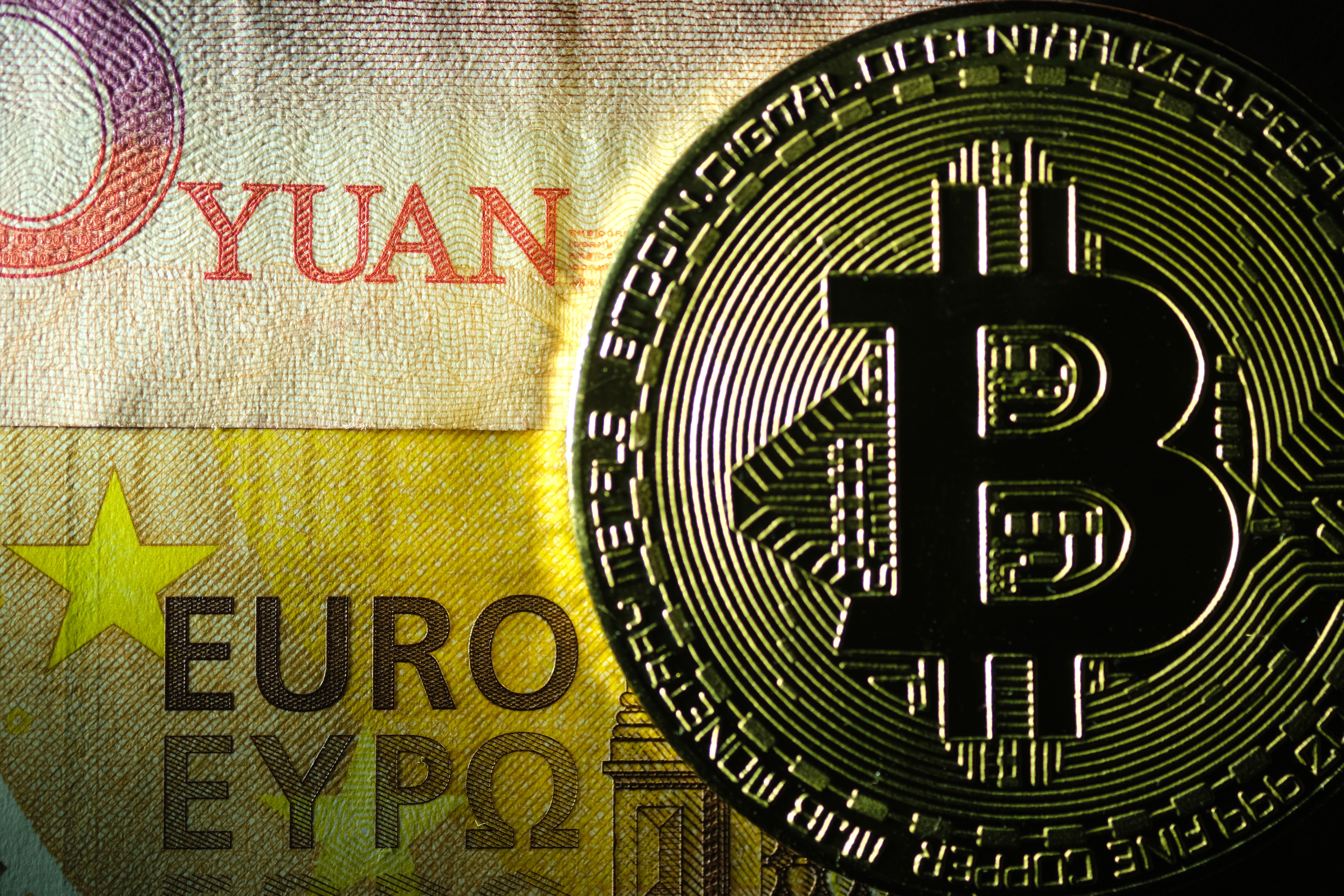 KATWIJK, NETHERLANDS - NOVEMBER 15: In this photo illustration, a visual representation of the digital Cryptocurrency, Bitcoin, is placed on top of an one hundred Chinese yuan banknote and a fifty euro banknote on November 15, 2020 in Katwijk, Netherlands. (Photo by Yuriko Nakao/Getty Images)