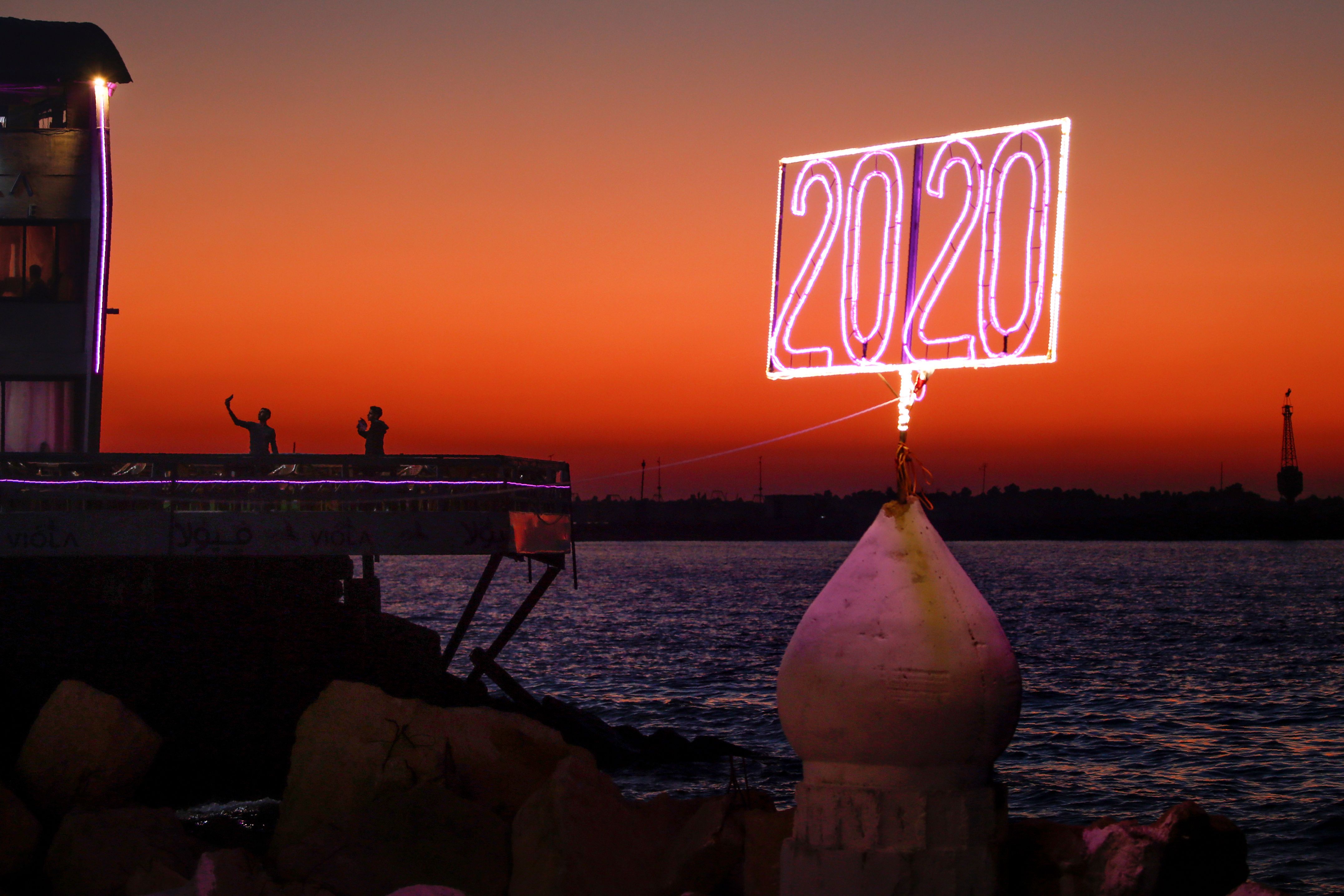 Palestinian youths pose for a "selfie picture" by the Mediterranean sea waterfront in Gaza City on December 23, 2019, a with a neon sign reading "2020" in the foreground.