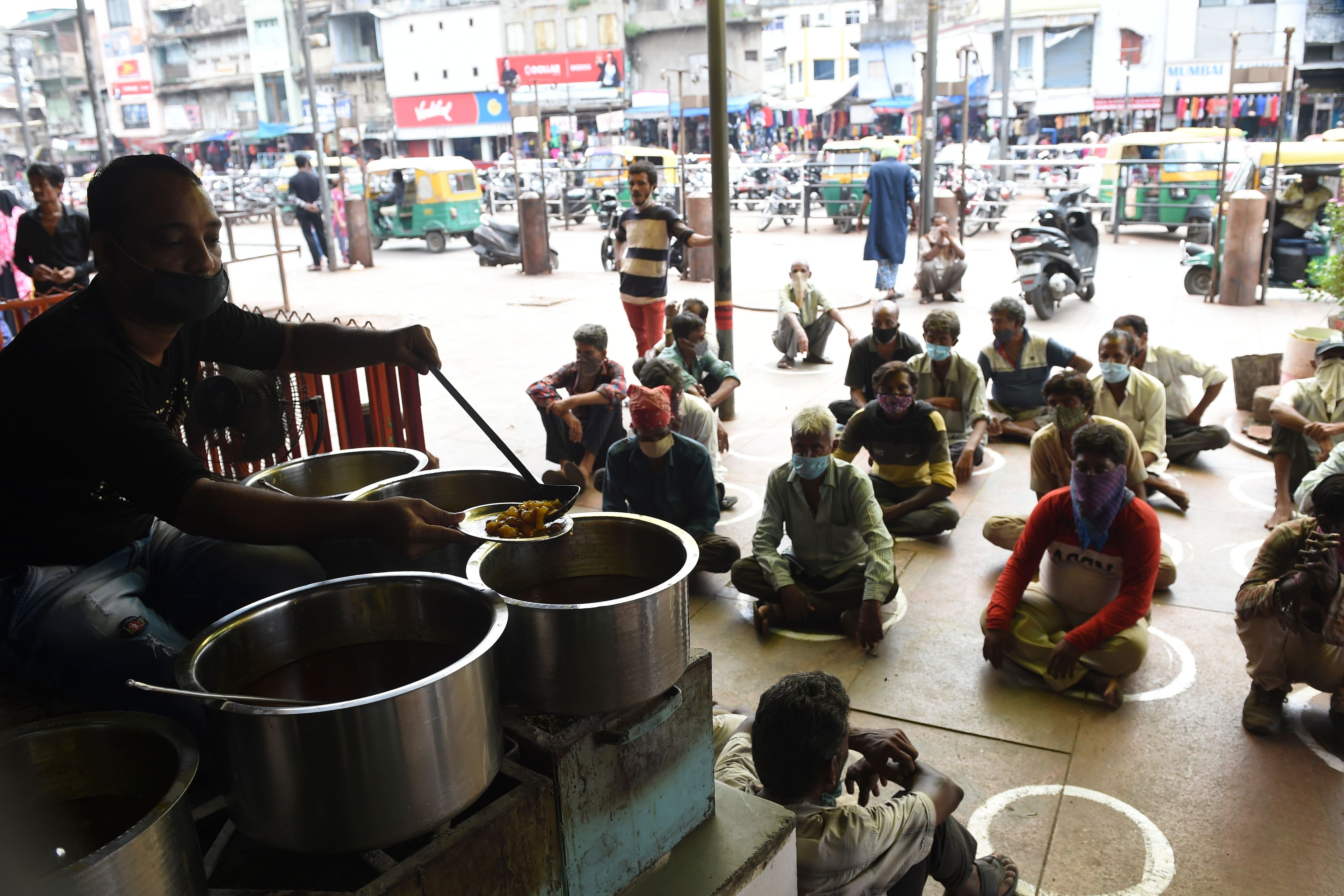 People in need sit while maintaining social distancing following Covid-19 Coronavirus guidelines, in front of a restaurant offering free meals in Ahmedabad on September 19, 2020. The number of people in extreme poverty has grown dramatically, according to the UN.