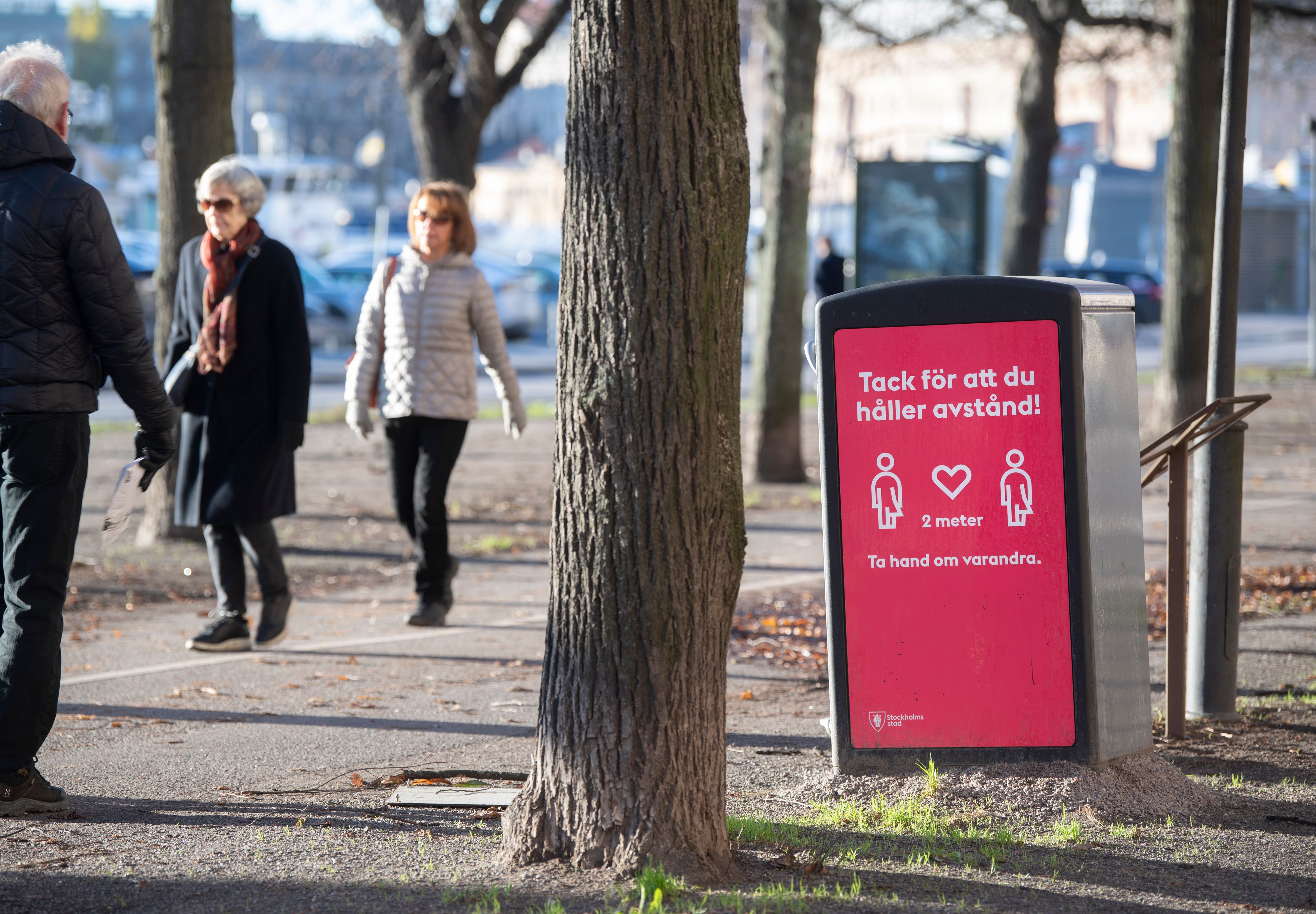 People strolling in the cold but sunny weather pass a sign asking to maintain social distancing, in Stockholm, Sweden, on November 20, 2020, amid the ongoing coronavirus pandemic.