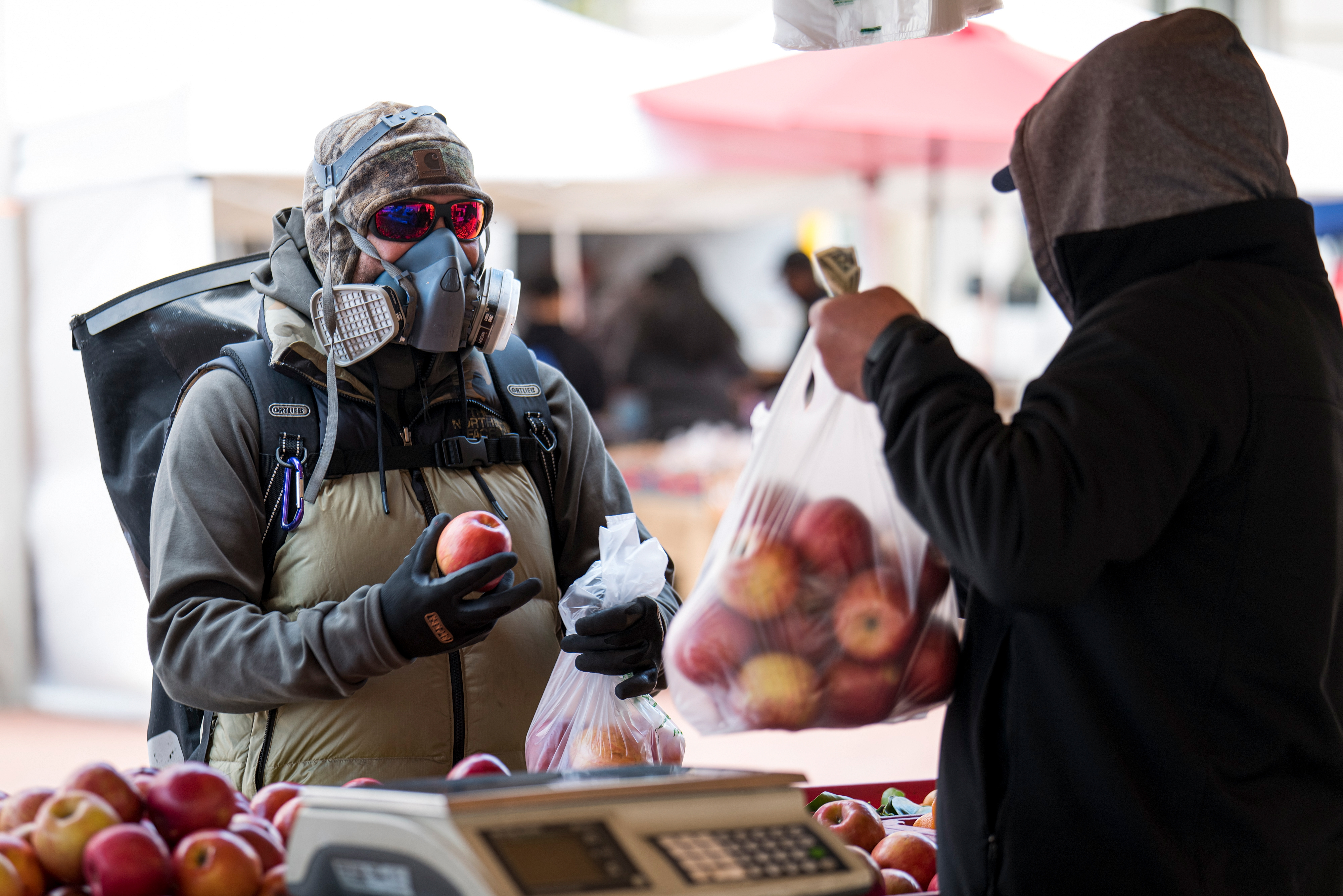 A customer wearing a protective face mask and gloves buys apples at a farmers’ market in San Francisco during the COVID-19 pandemic, on March 25, 2020.